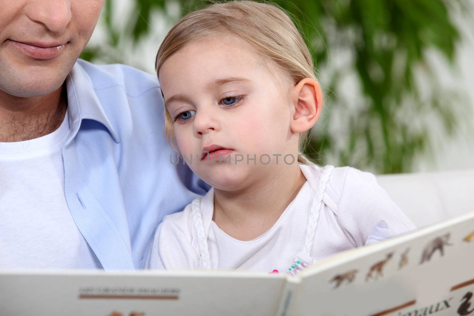 Father and daughter reading book by phovoir