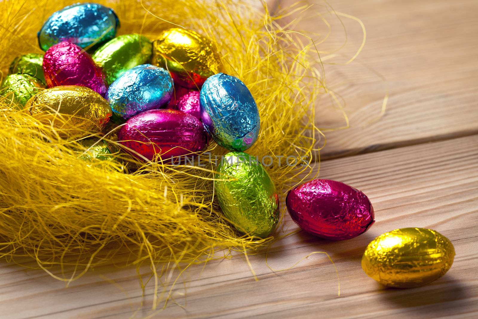 Chocolate easter eggs in yellow nest on wooden table background. Holiday composition