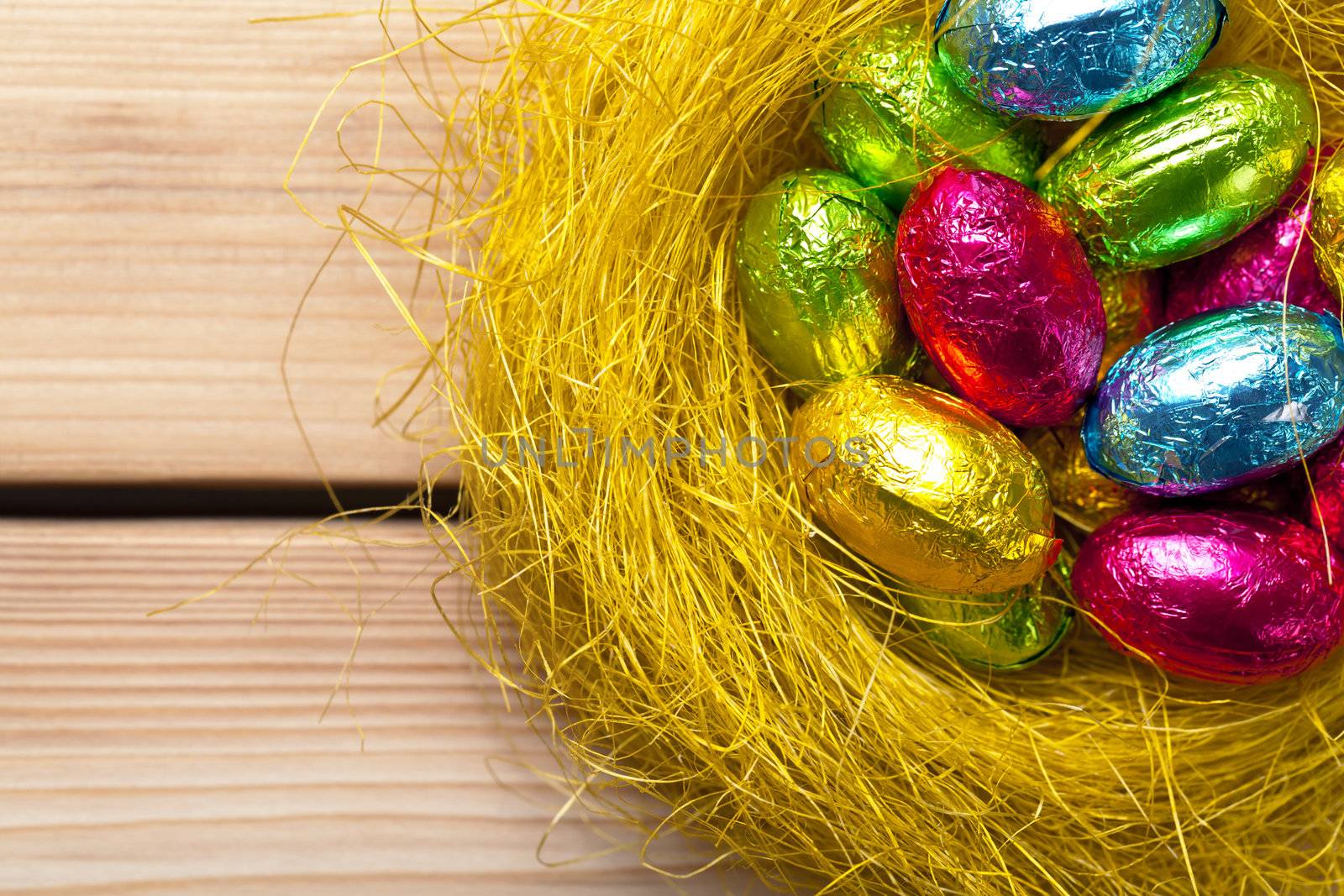 Easter eggs in yellow nest on wooden background. Holiday composition. Top view