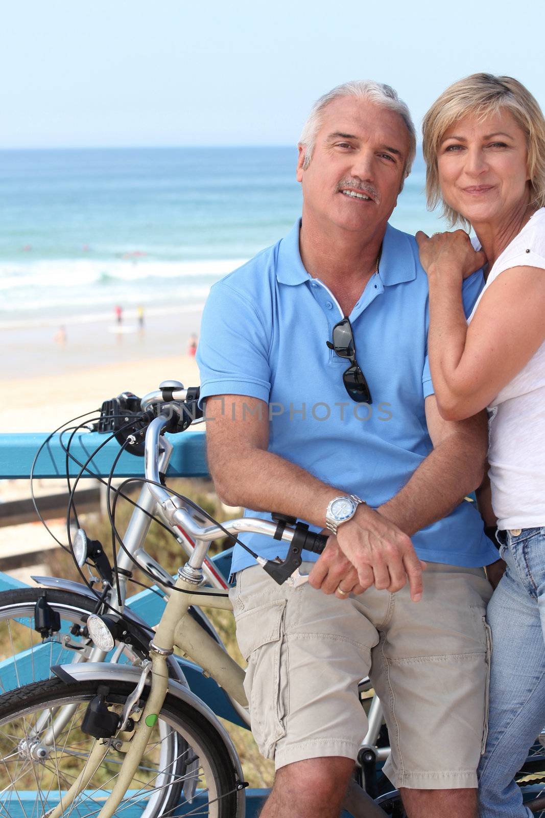 A middle aged couple biking by the seashore.