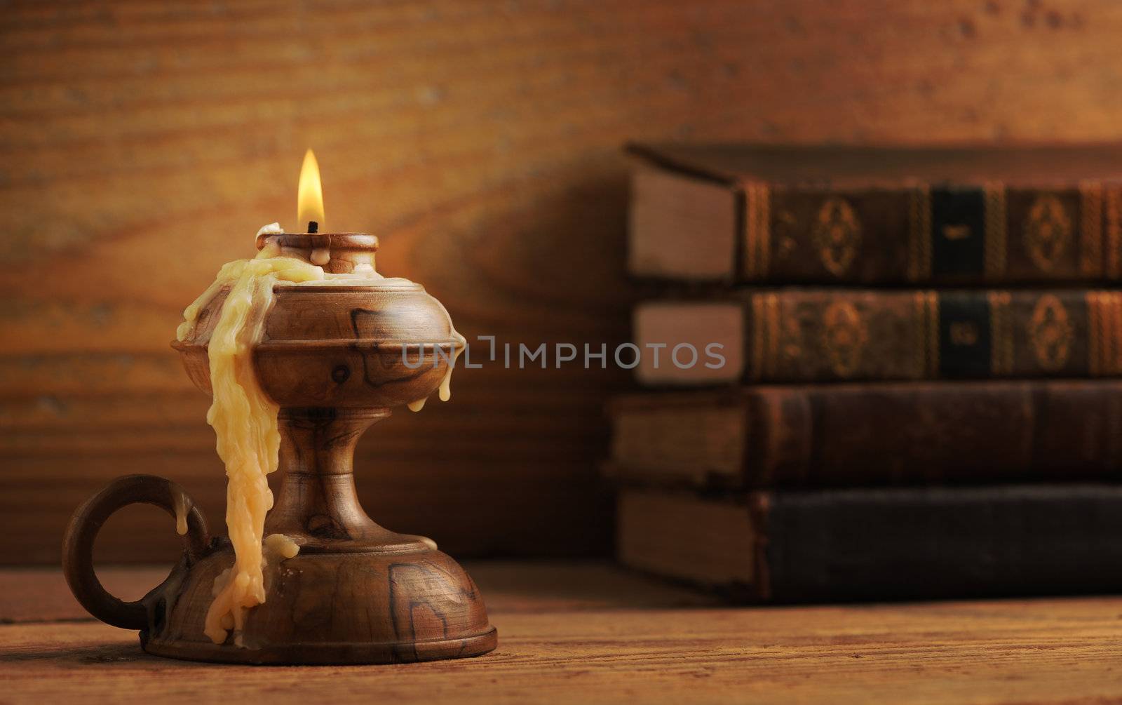 old candle on a wooden table, old books in the background by stokkete