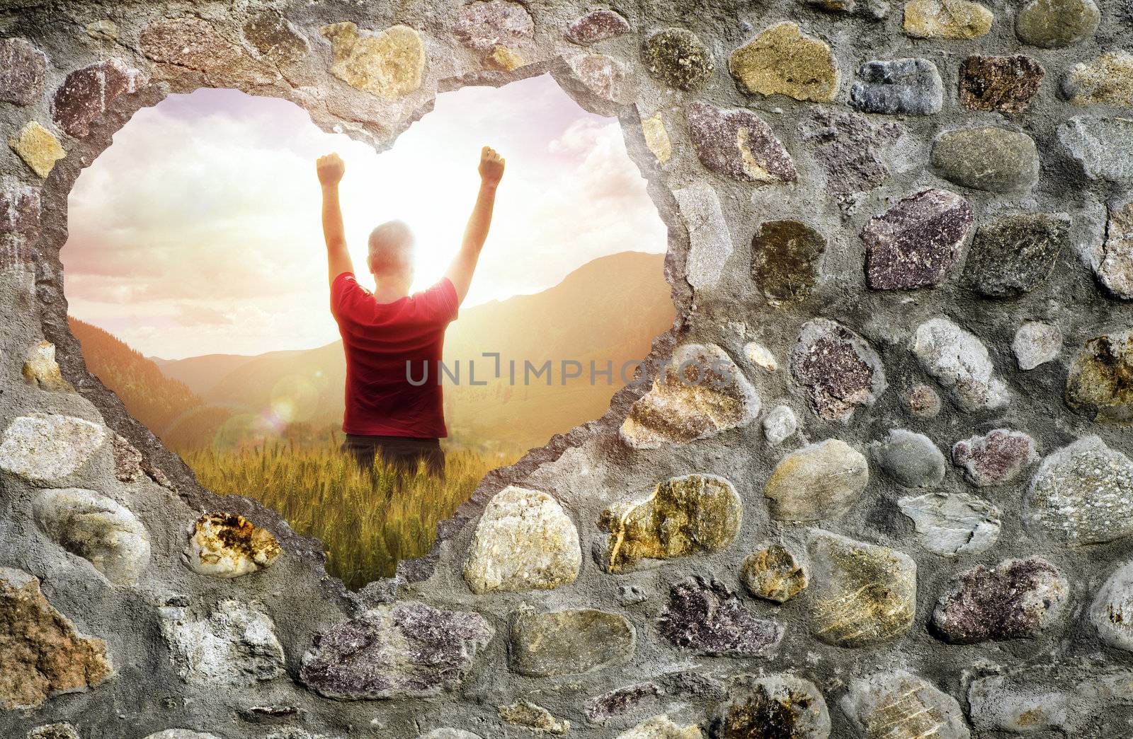 Broken stone wall in a shape of heart and a young man raising his hands up