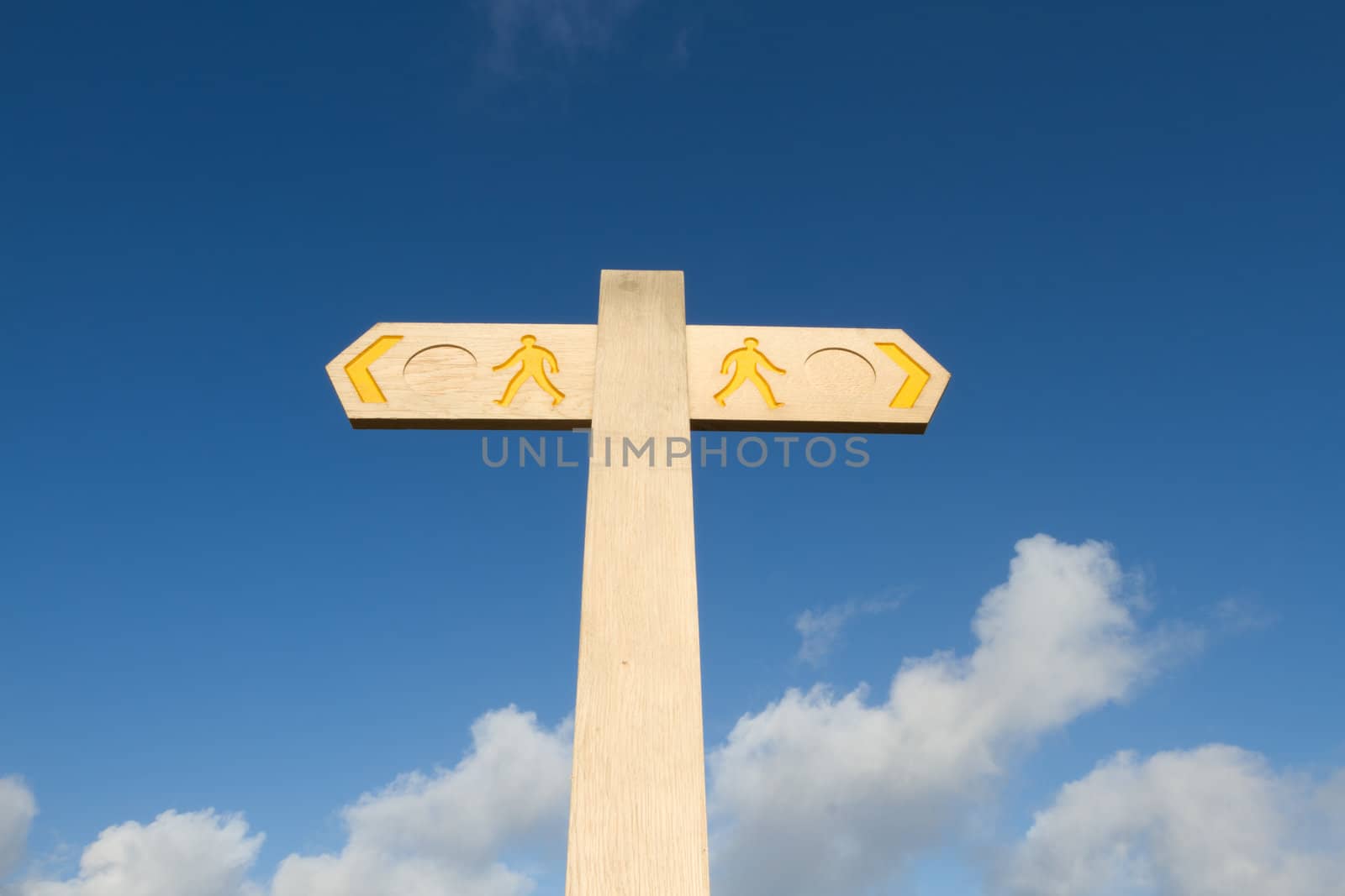 A wooden post with dual direction arrows and figures of people coloured in yellow against a brilliant blue sky with white cloud.
