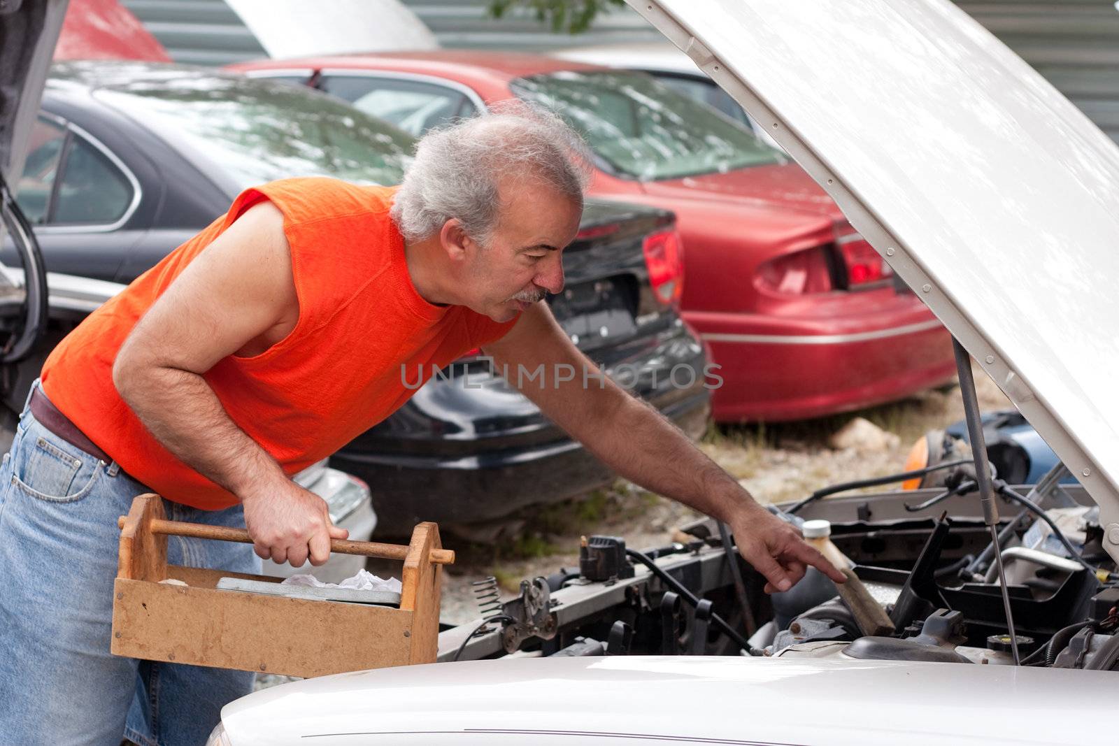 A man looking for car parts on decommissioned junk cars at an automotive scrap yard.