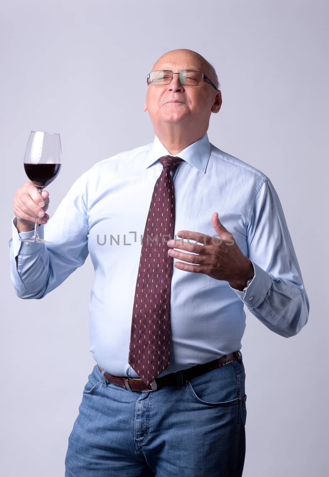 portrait of a successful senior man with glass of wine on gray background
