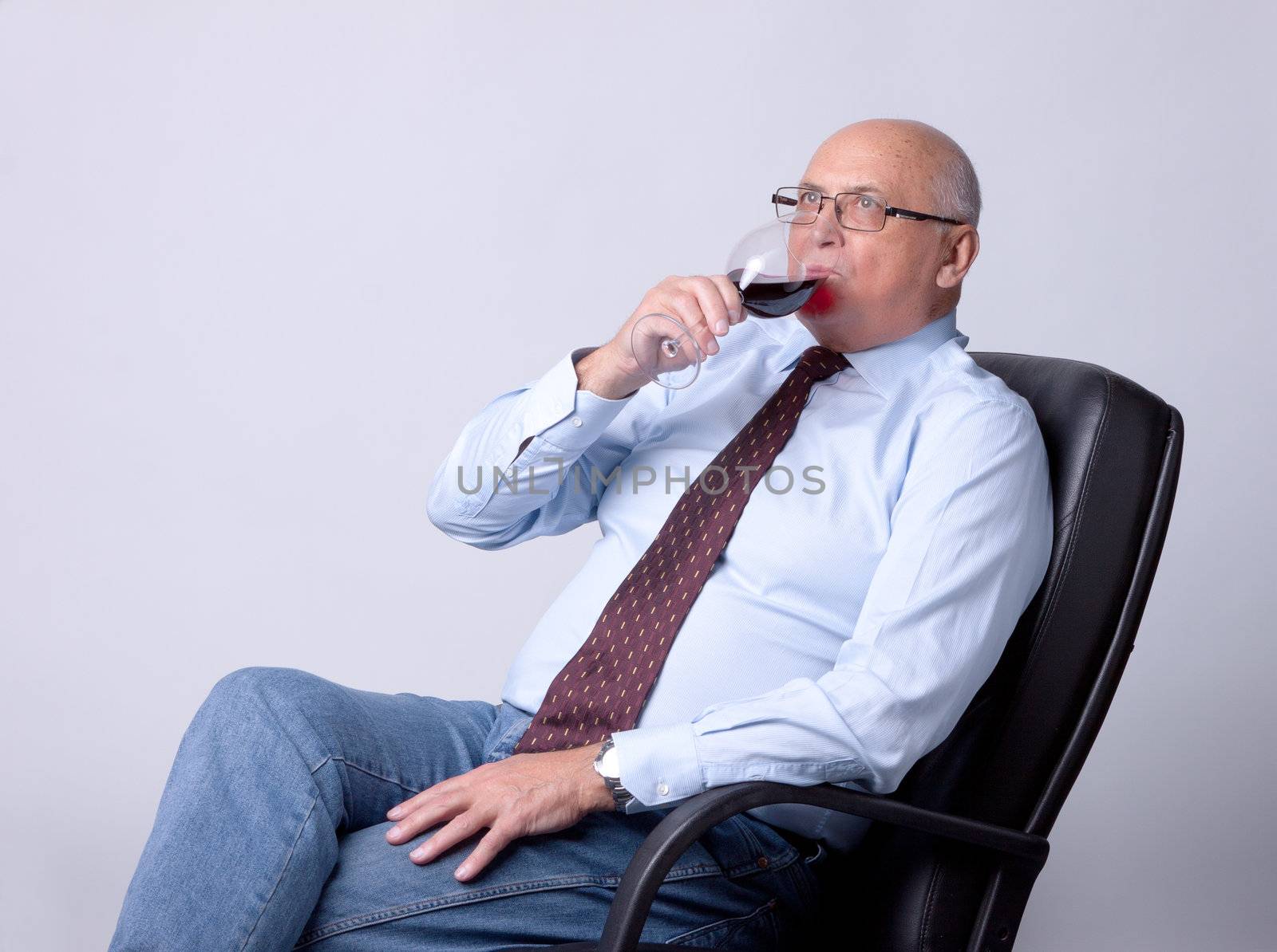 portrait of a successful senior man with glass of wine on gray background