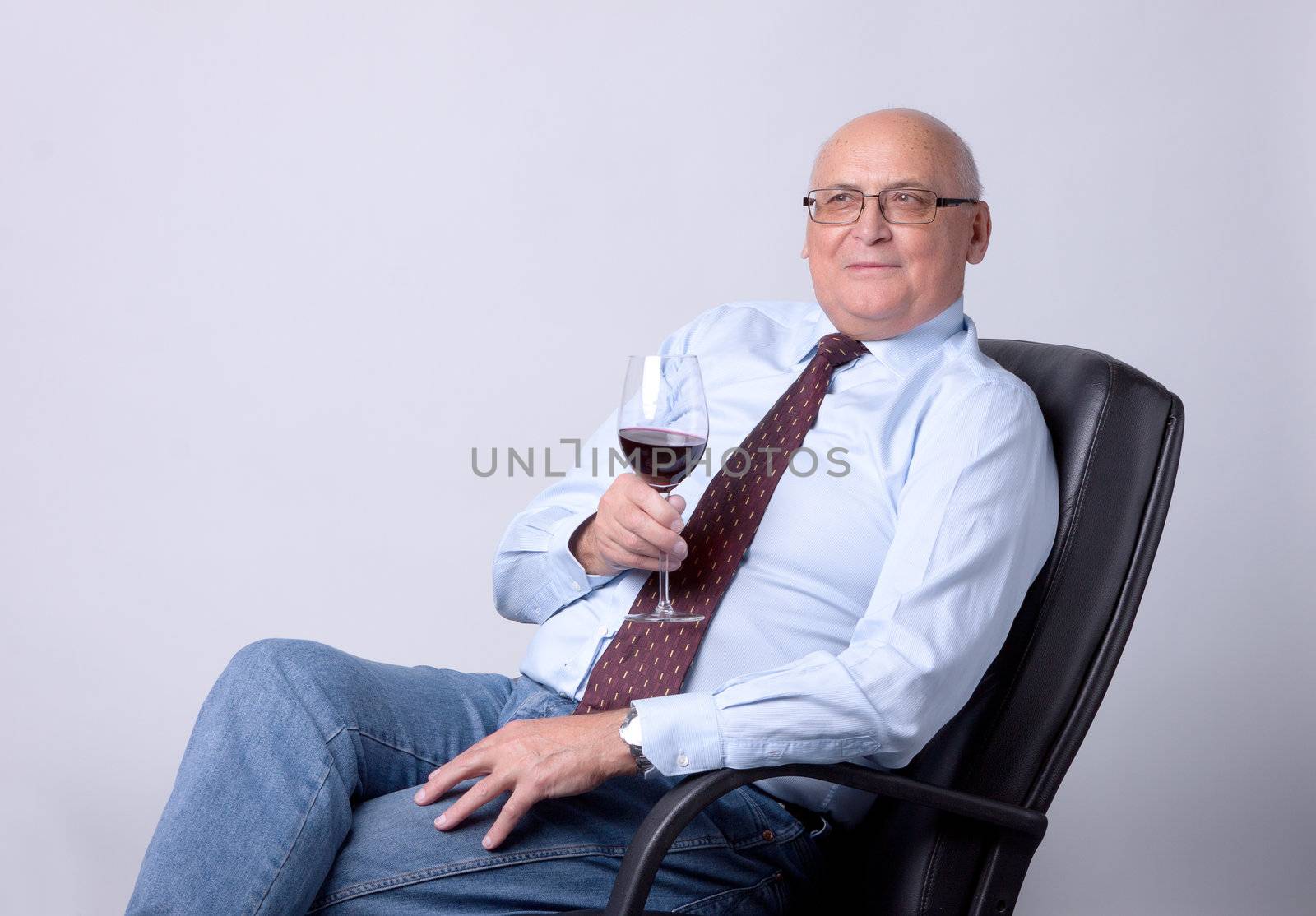 portrait of a successful senior man with glass of wine on gray background