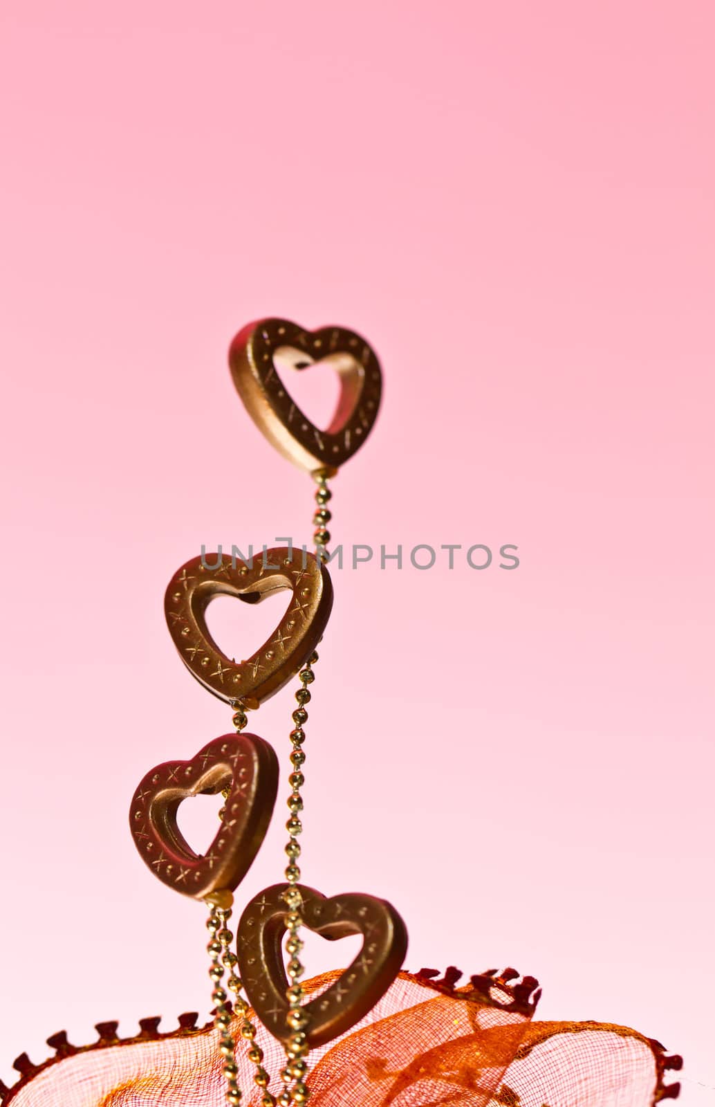 four plastic valentine hearts at left frame on pink background in portrait orientation