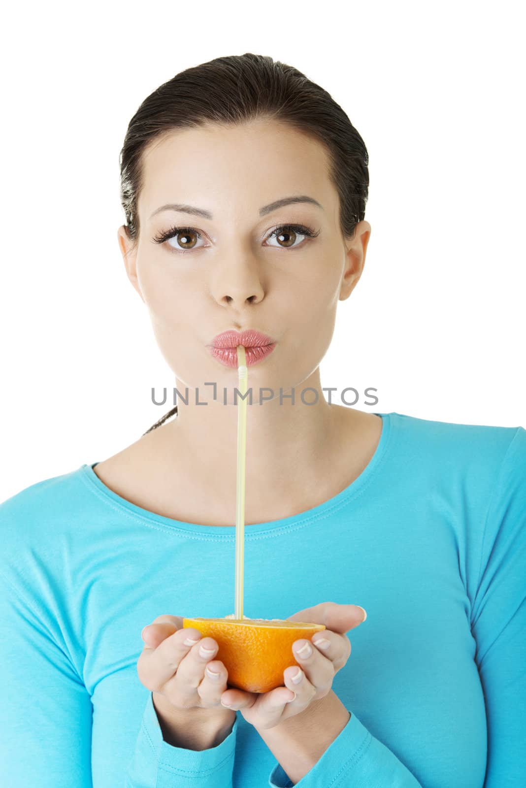 Attractive smiling young woman drinking orange juice straight from fruit