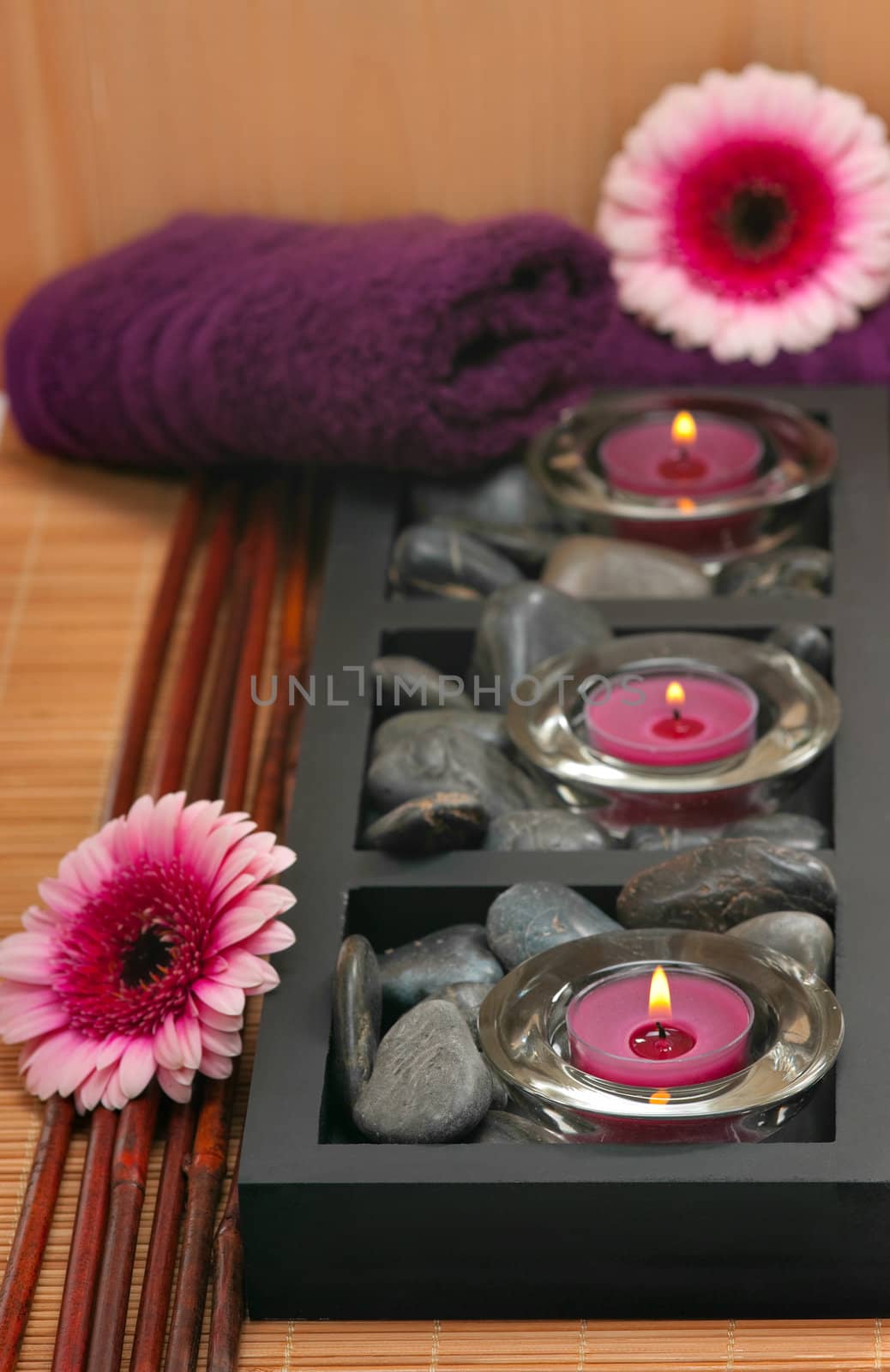 Spa scene with aromatic candles, daisy gerberas and healing pebbles
