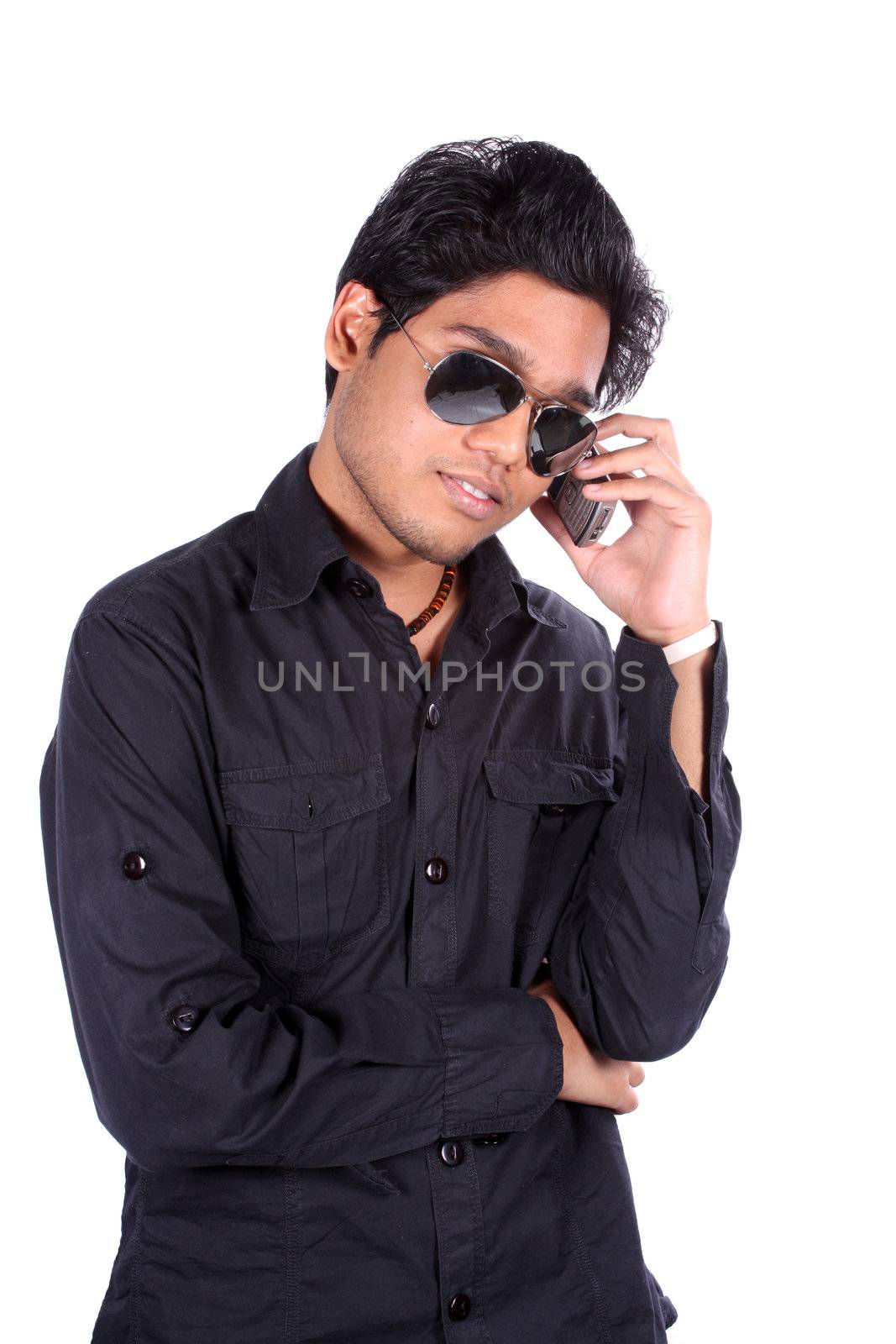 A young Indian man wearing sunglasses talking on the phone, on white studio background.