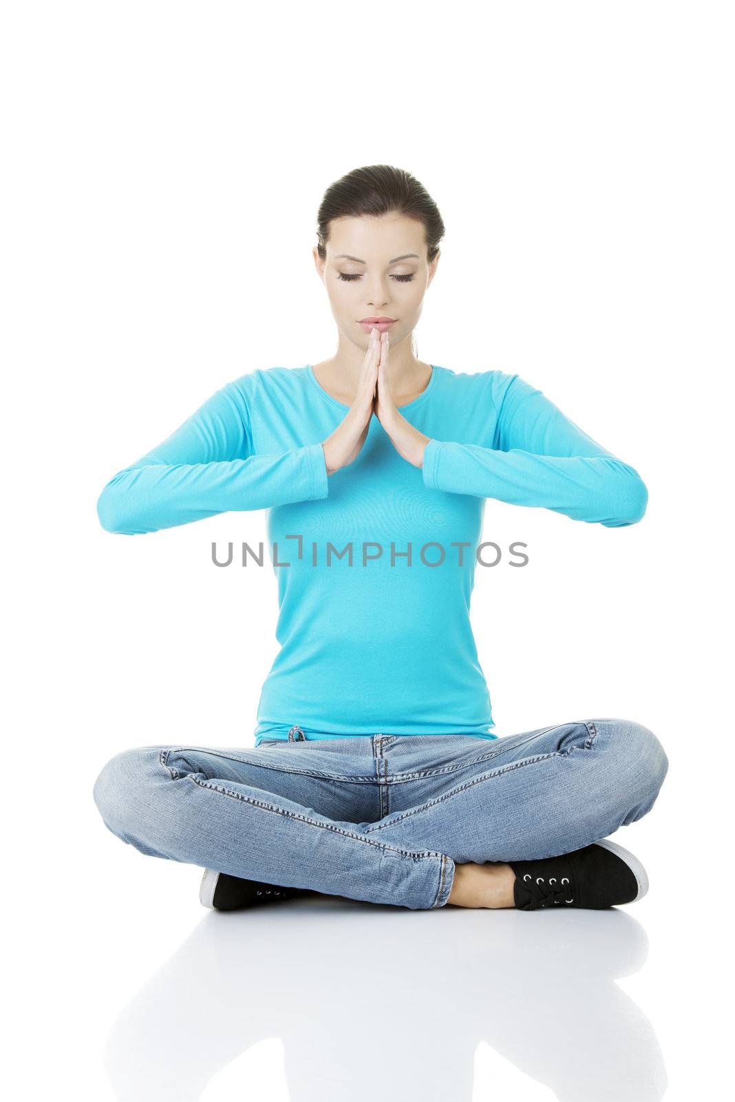 Portrait of young pretty student girl over white background meditating in lotus pose. She is relaxed and concentrated
