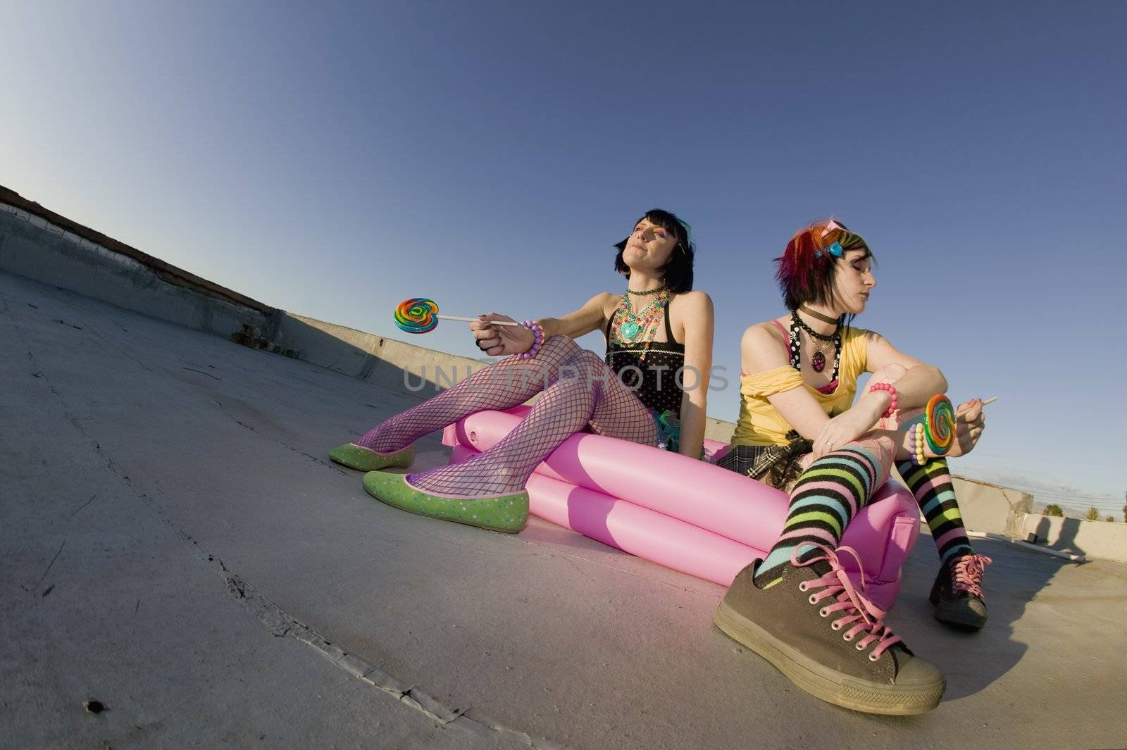 Fisheye shot of girls in brightly colored clothing in a plastic pool on a roof with sunglasses and lollipops