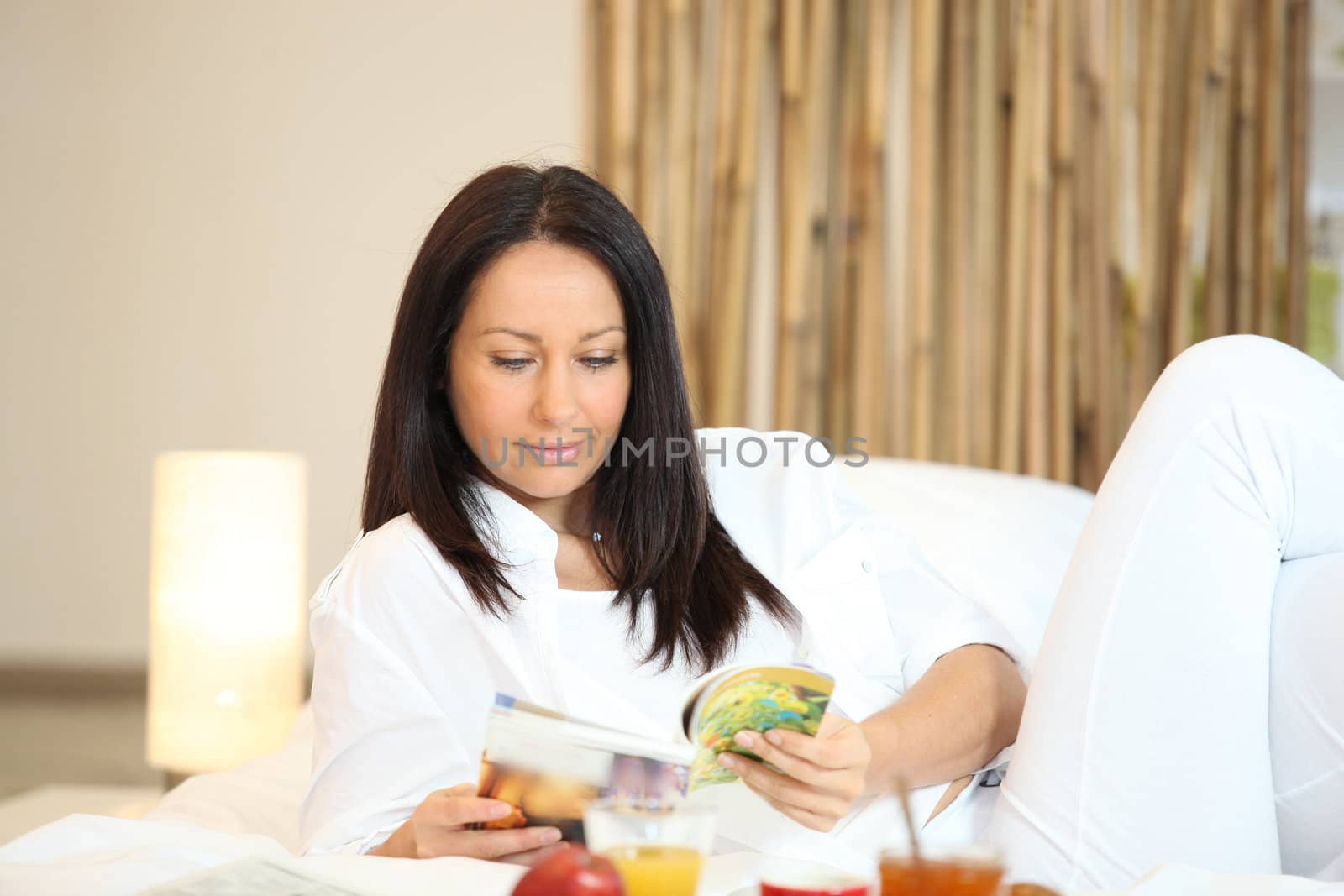 Woman reading a magazine over breakfast by phovoir