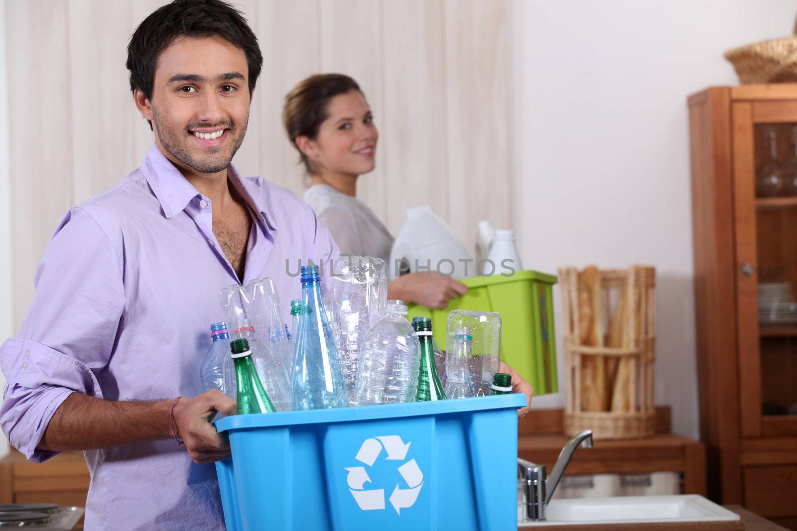 a young couple recycling plastic in their kitchen by phovoir