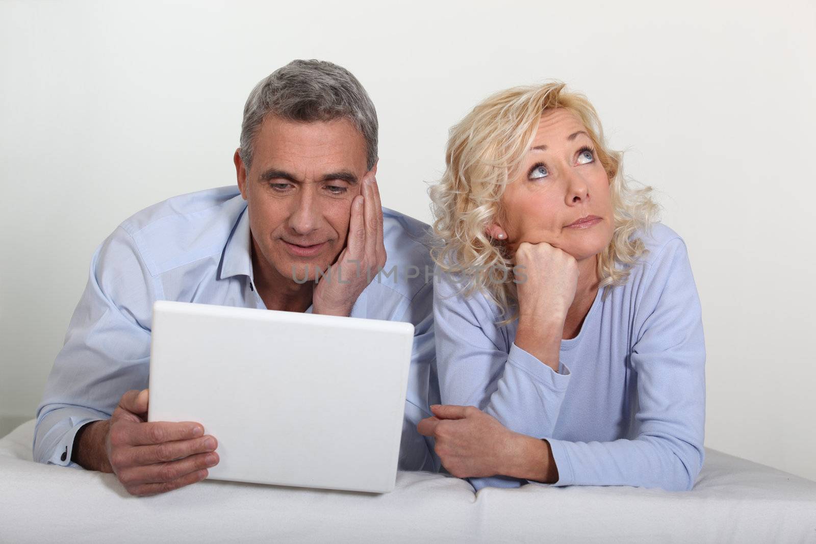 Middle aged couple with a laptop on their bed. by phovoir