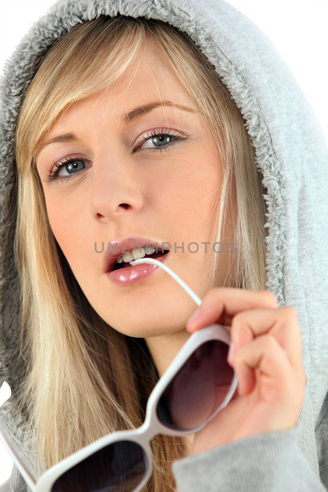 Woman in a hooded sweatshirt biting her sunglasses