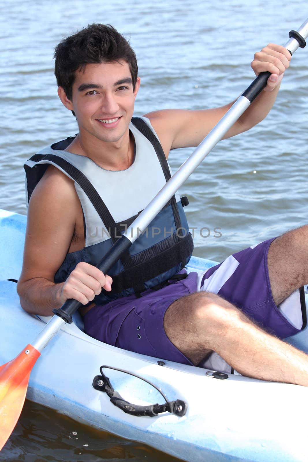 Young man paddling a kayak by phovoir