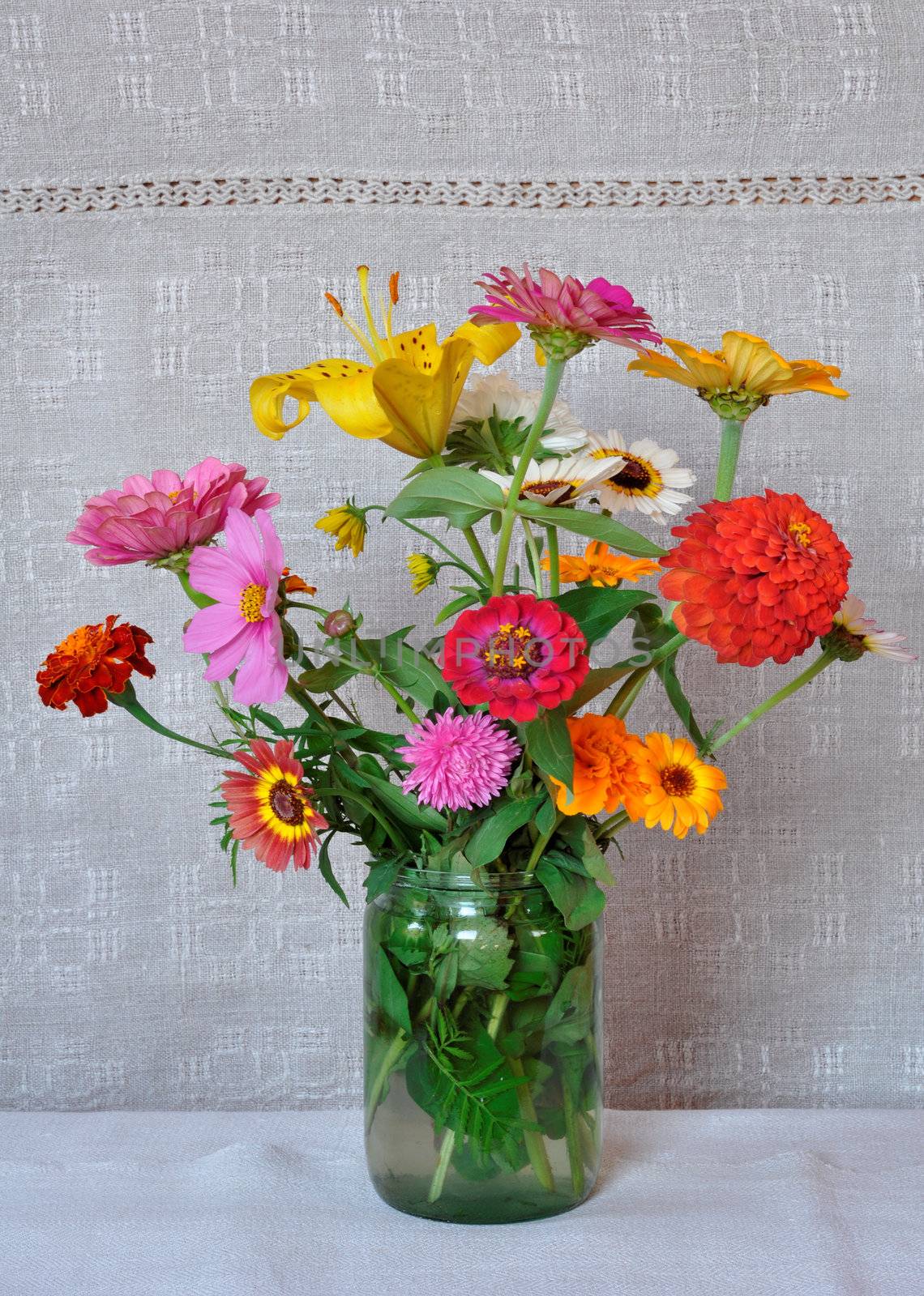 A bouquet of garden flowers in a glass jar on the background of an old linen canvas. August, the Central Russia