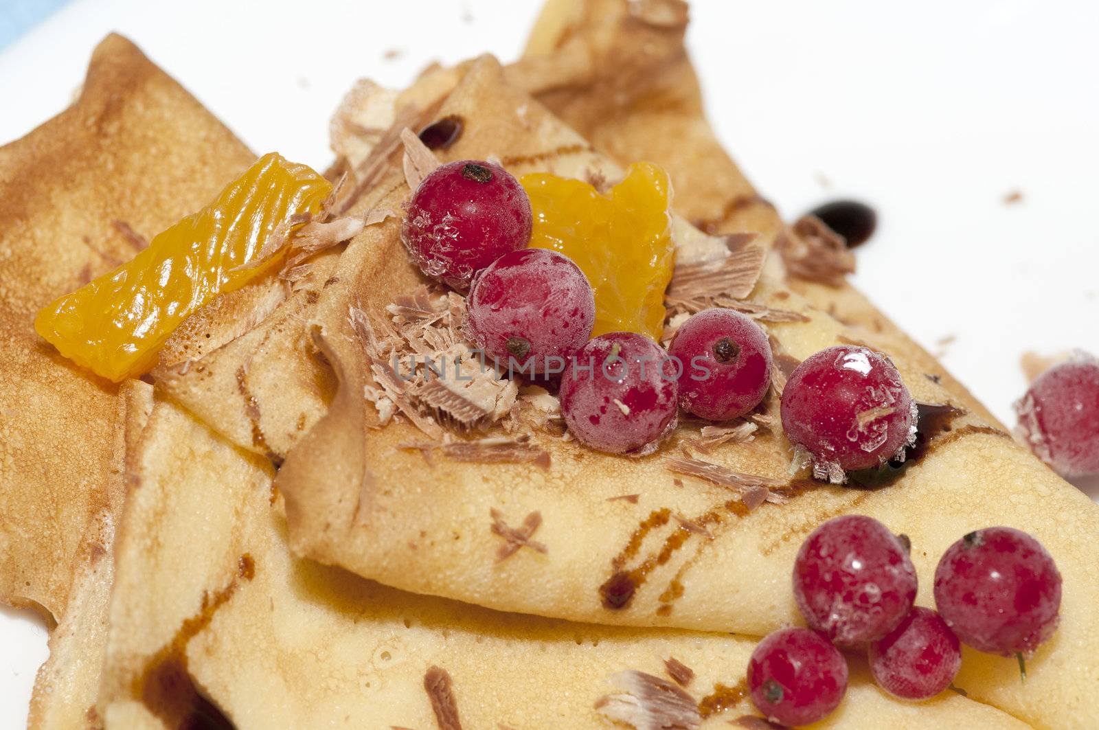 Pancakes with orange, shaving chocolate and red currants close up
