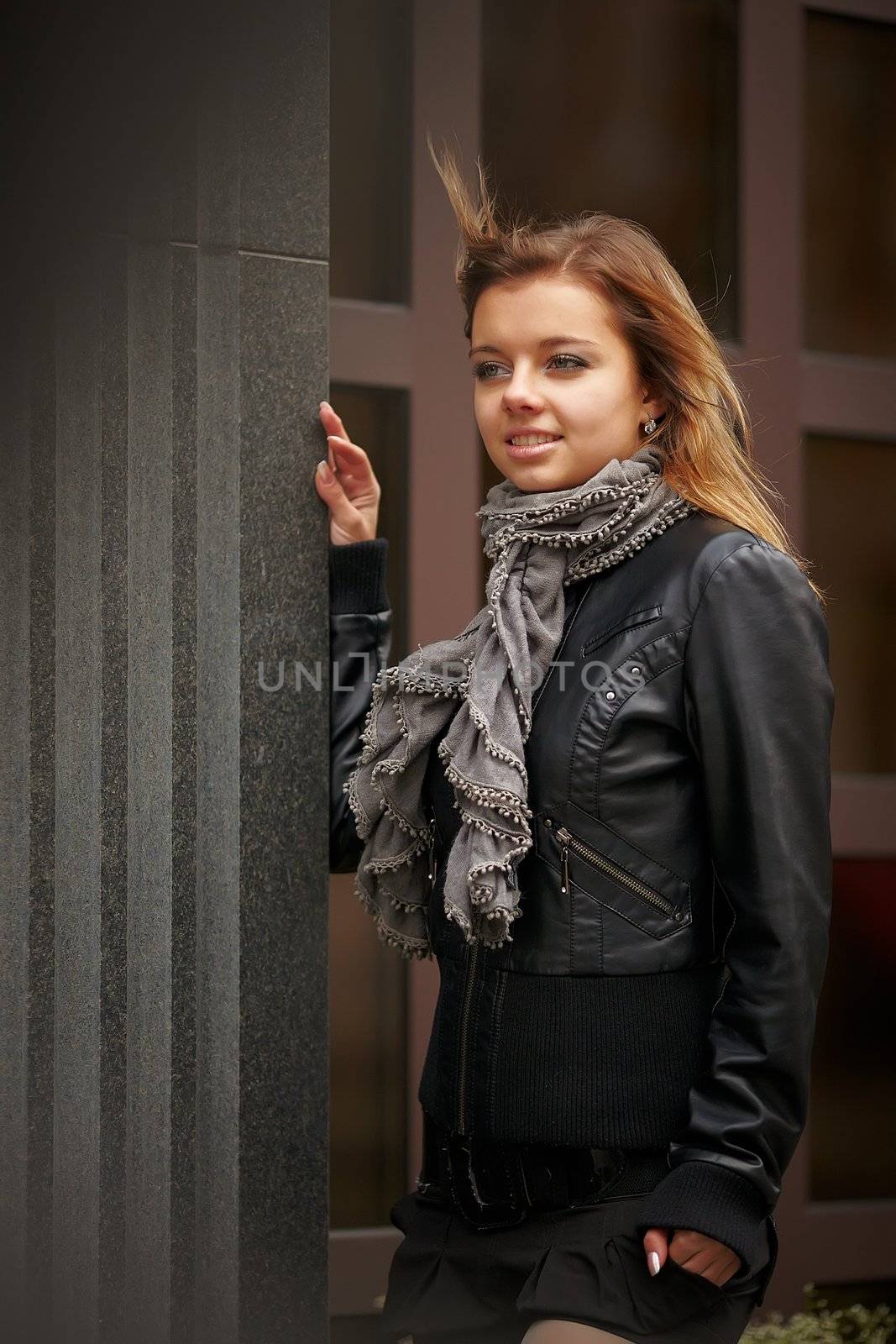 Beautiful girl in autumn coat standing near expensive granite facade. Wind waving her hair beautifully. girl smiling