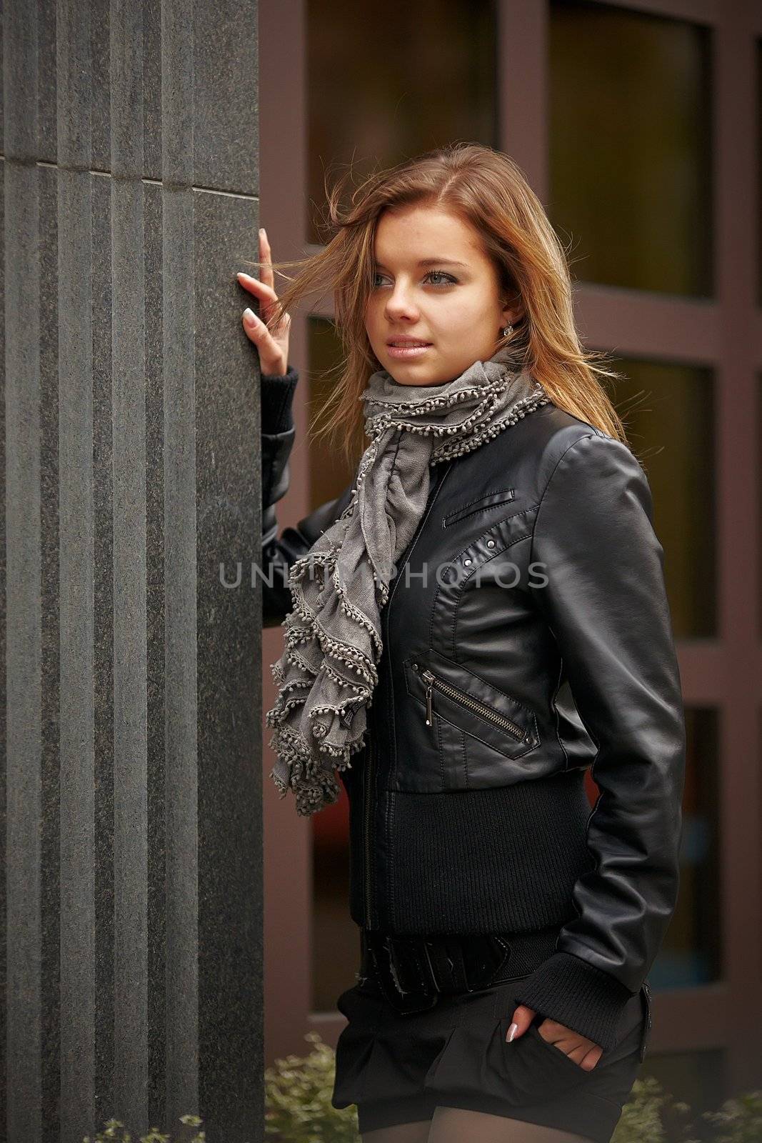 Beautiful girl in autumn coat standing near expensive granite facade. Wind waving her hair beautifully. girl smiling