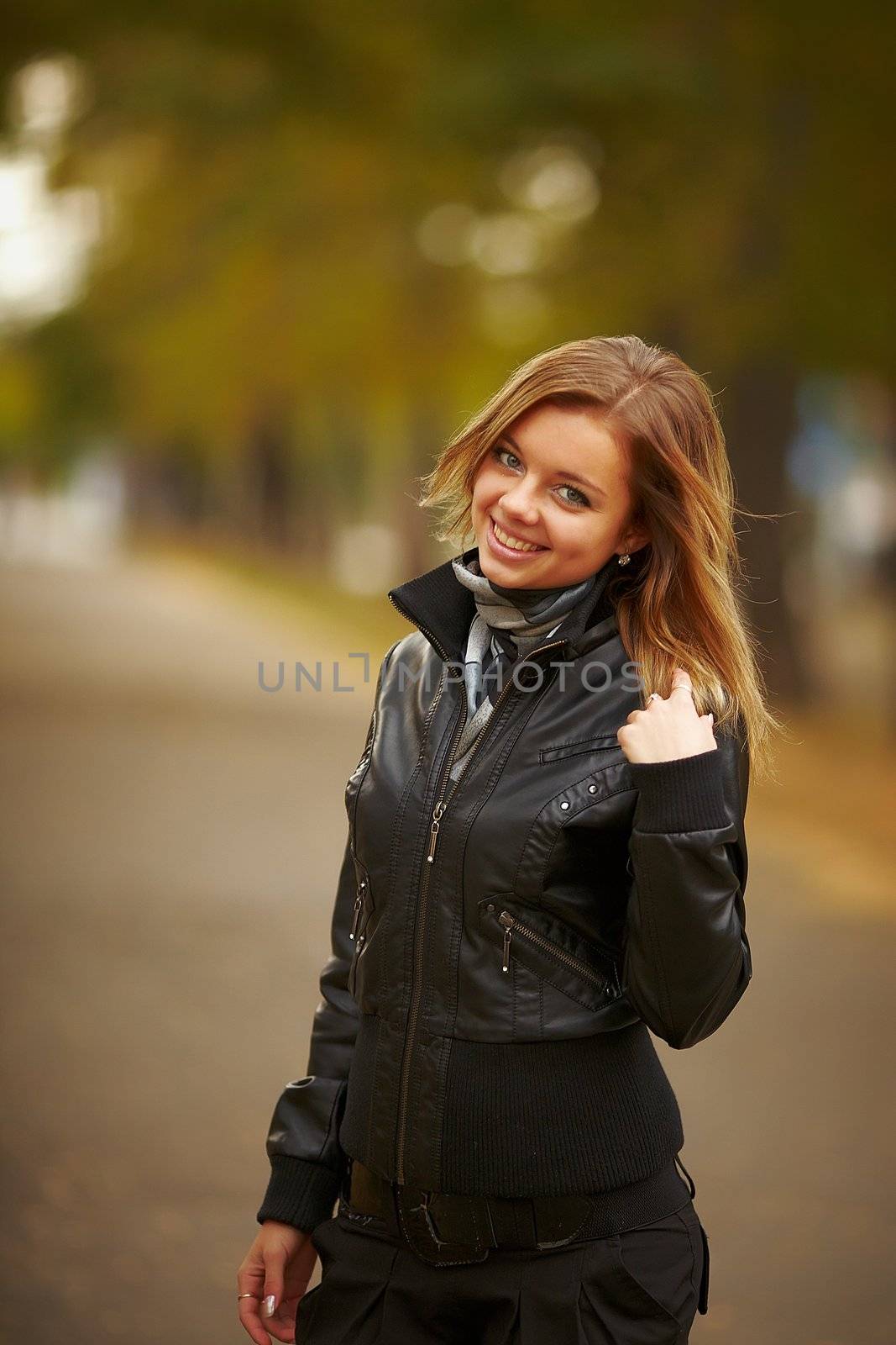 Beautiful and cheerful girl walking in autumn park. Is on aleykii, turns around and smiles