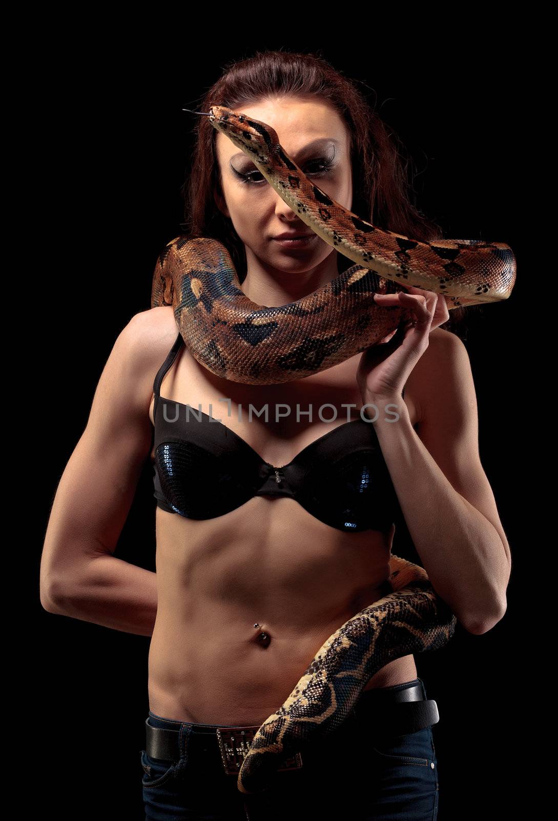 Mysterious beautiful exotic woman with a boa entwined around her body standing in shadows on a dark background