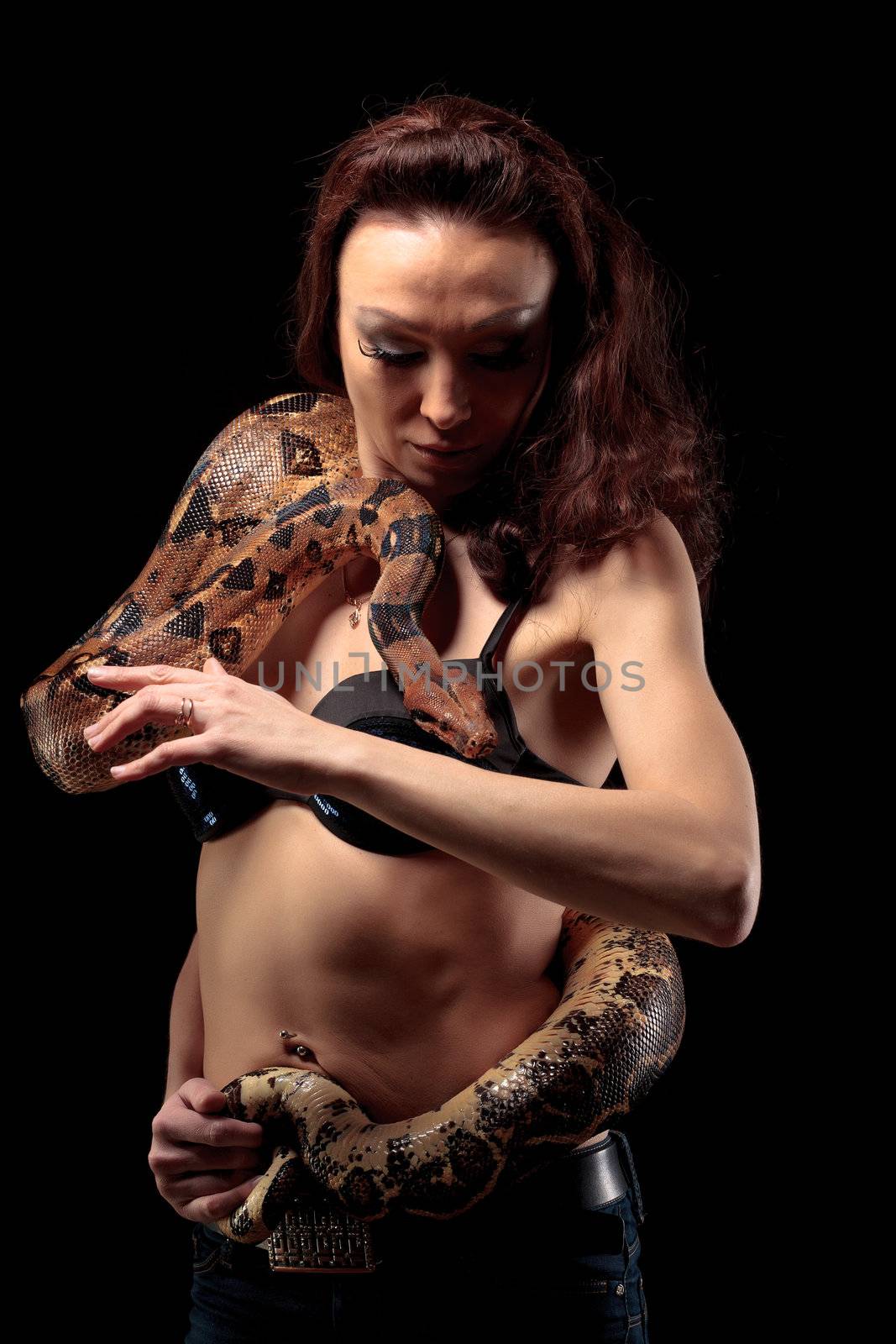 Mysterious beautiful exotic woman with a boa entwined around her body standing in shadows on a dark background
