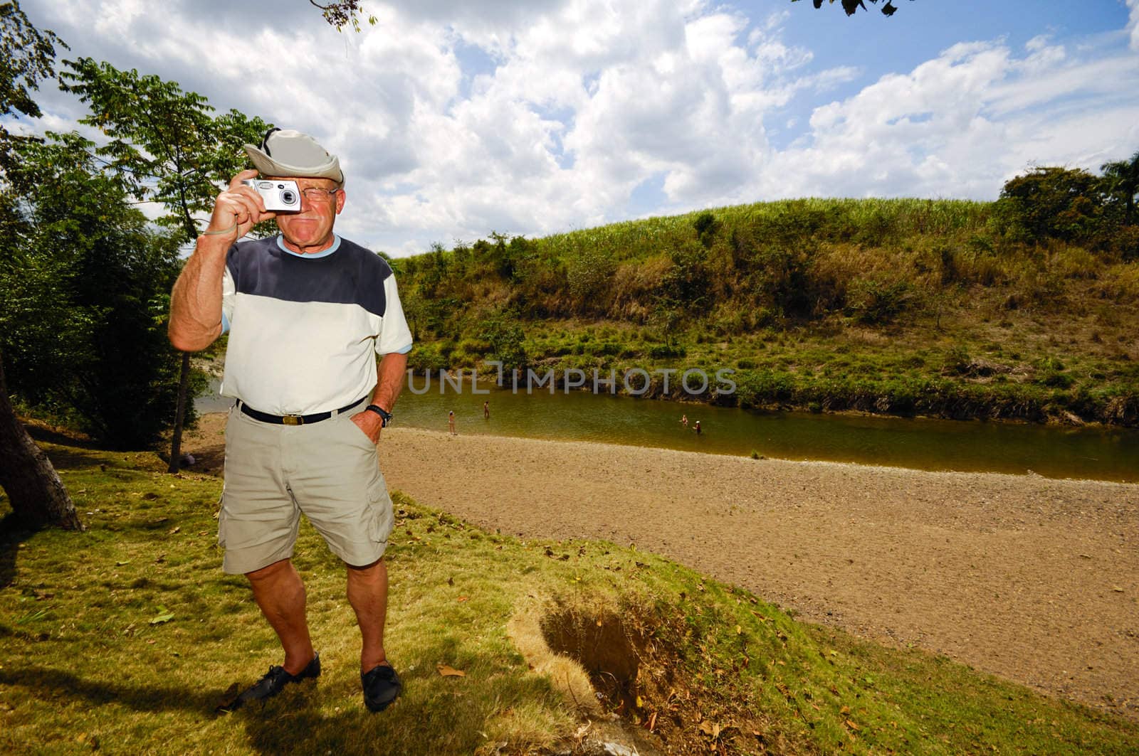 A tourist is standing in green nature. The man is a senior and is holding a camera. Dominican Republic.