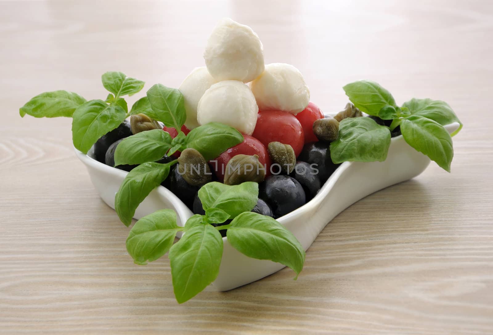 Appetizer of mozzarella, cherry tomatoes and olives, basil and capers