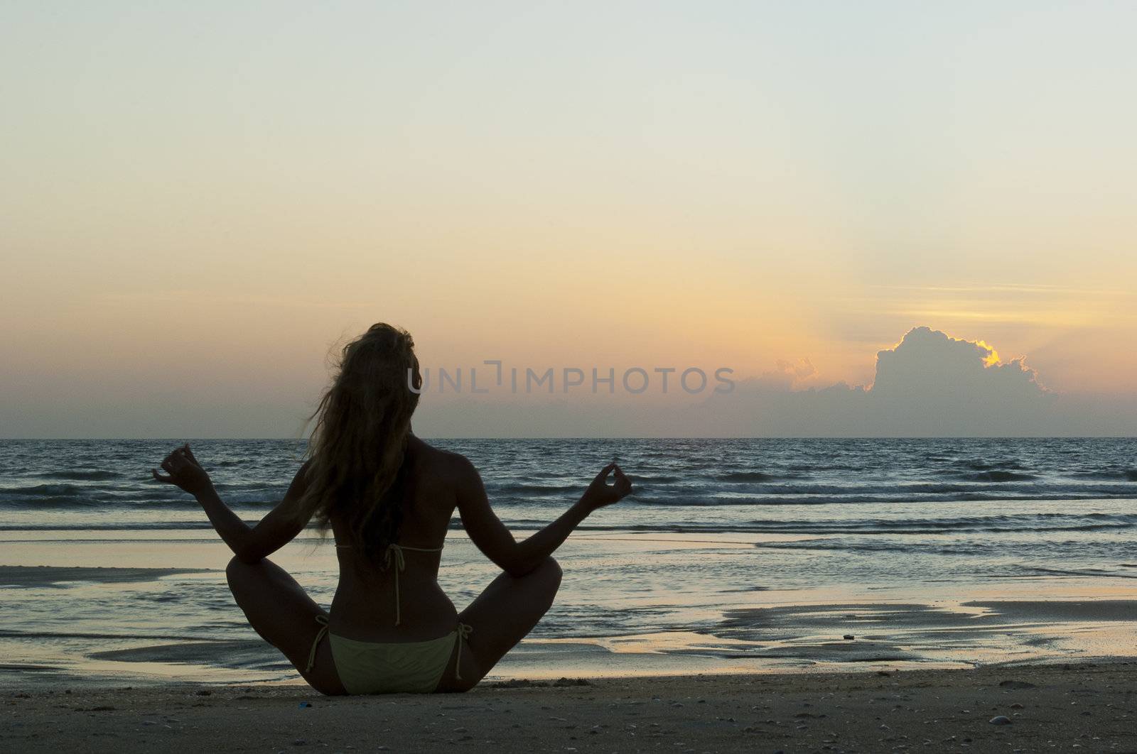 Meditating woman on the beach at sunset by Denovyi
