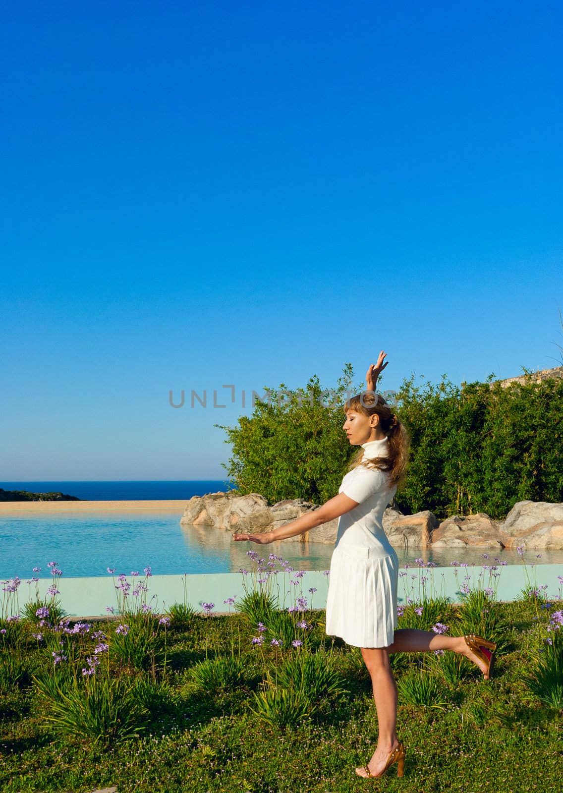 Beautiful woman in white dress meditating near water