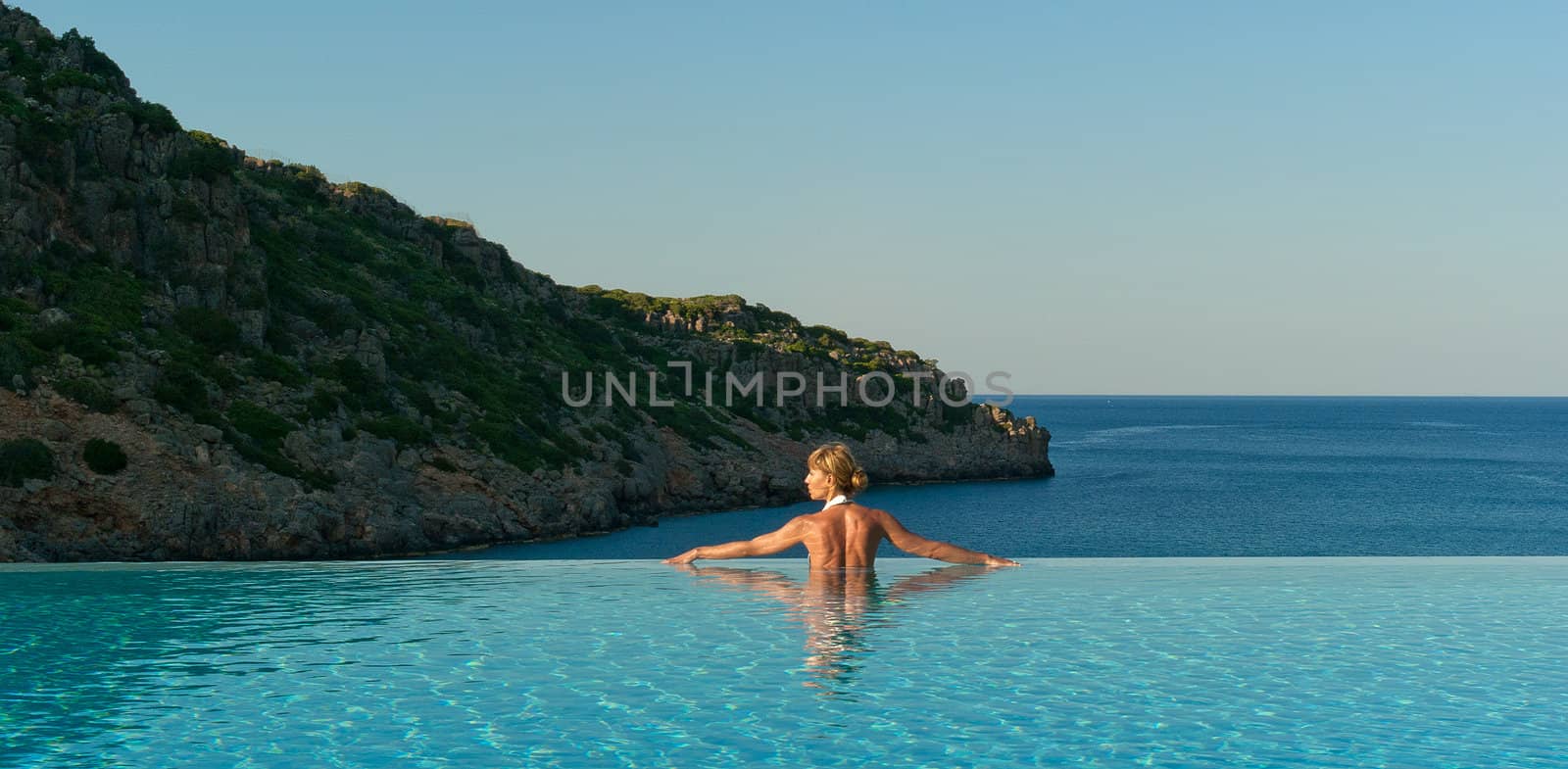 Beautiful woman relaxing in infinity swimming pool near coast 