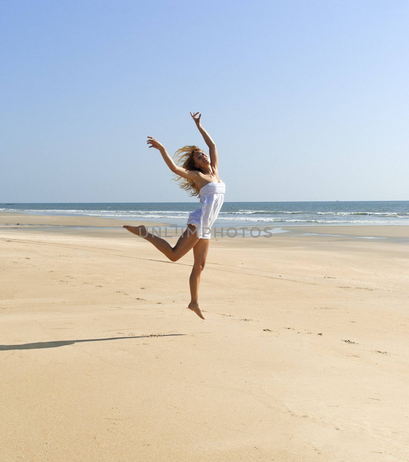 Happy beautiful woman jumping on sunny beach