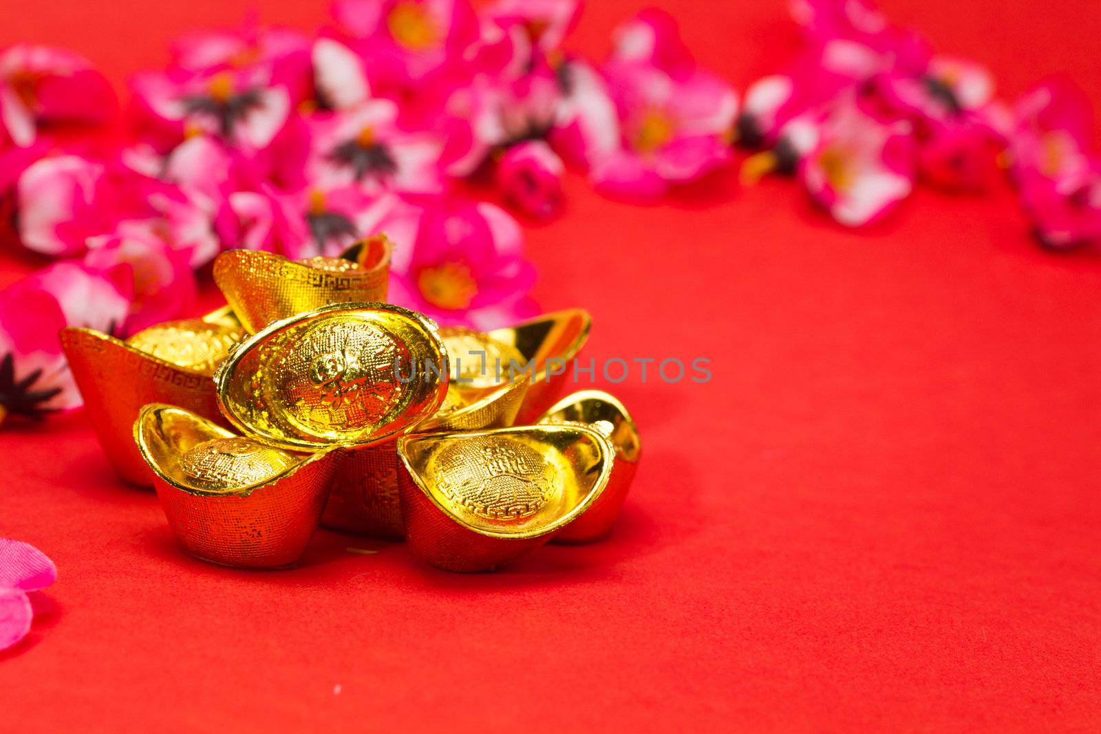 Golden Chinese New Year Ingots on red surface with plum blossoms in background