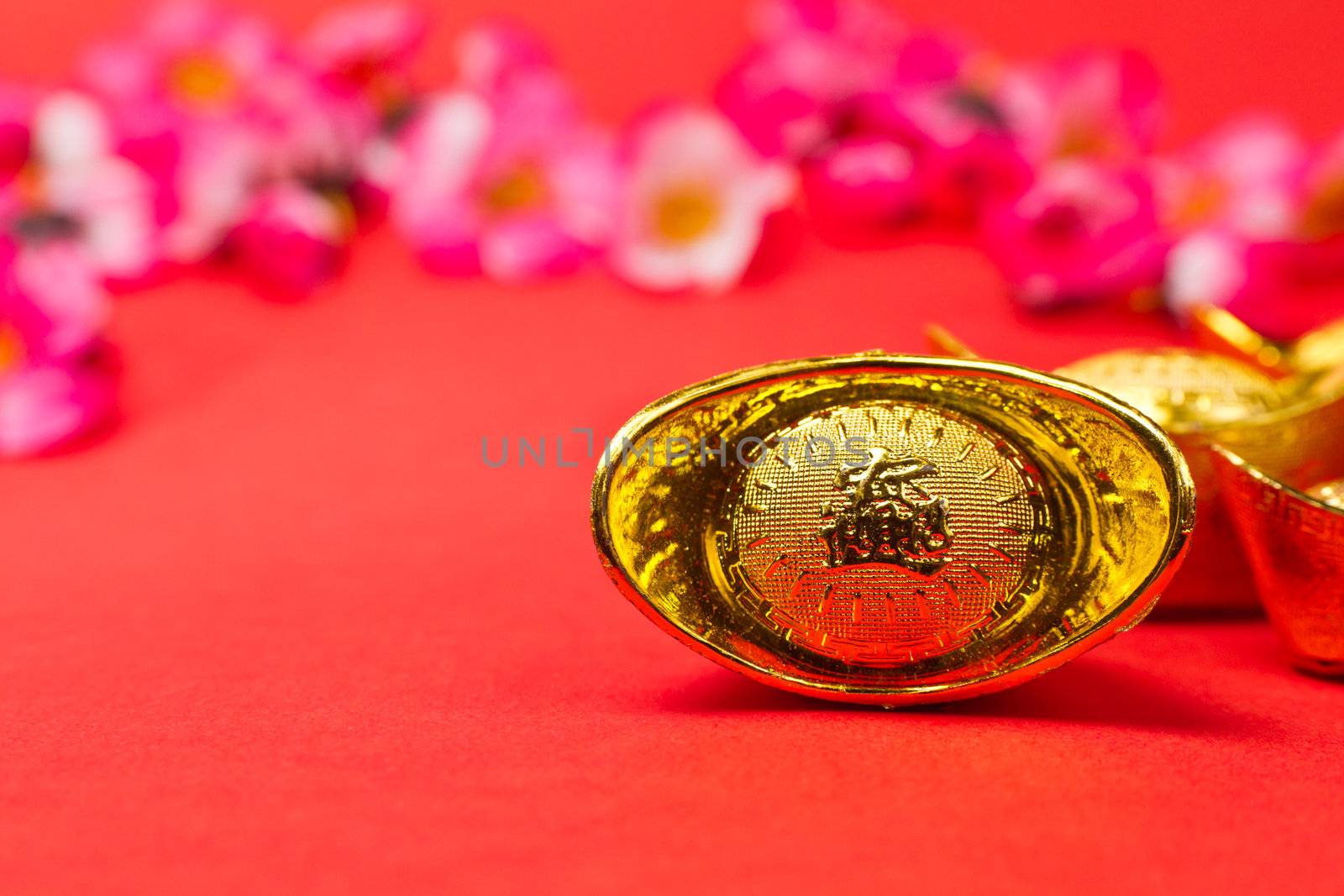 Golden Chinese new Year Ingots on red surface with plum blossoms in background