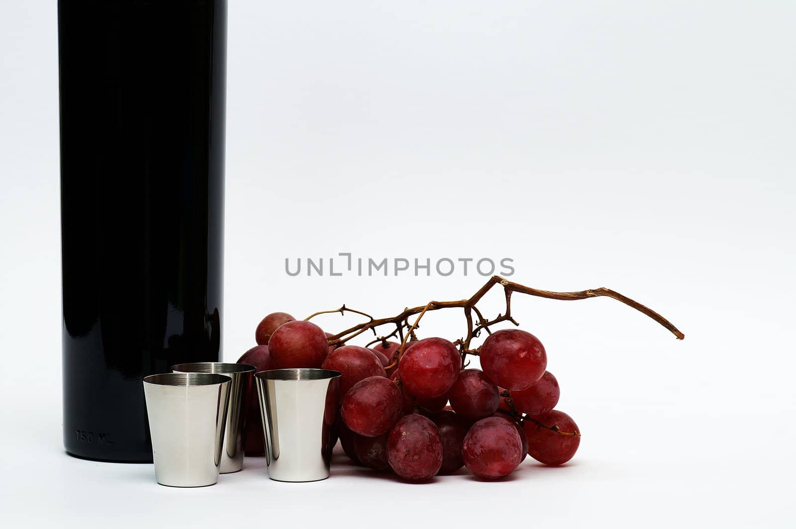 Three steel cups in front of red grape branch and a part of red vine bottle