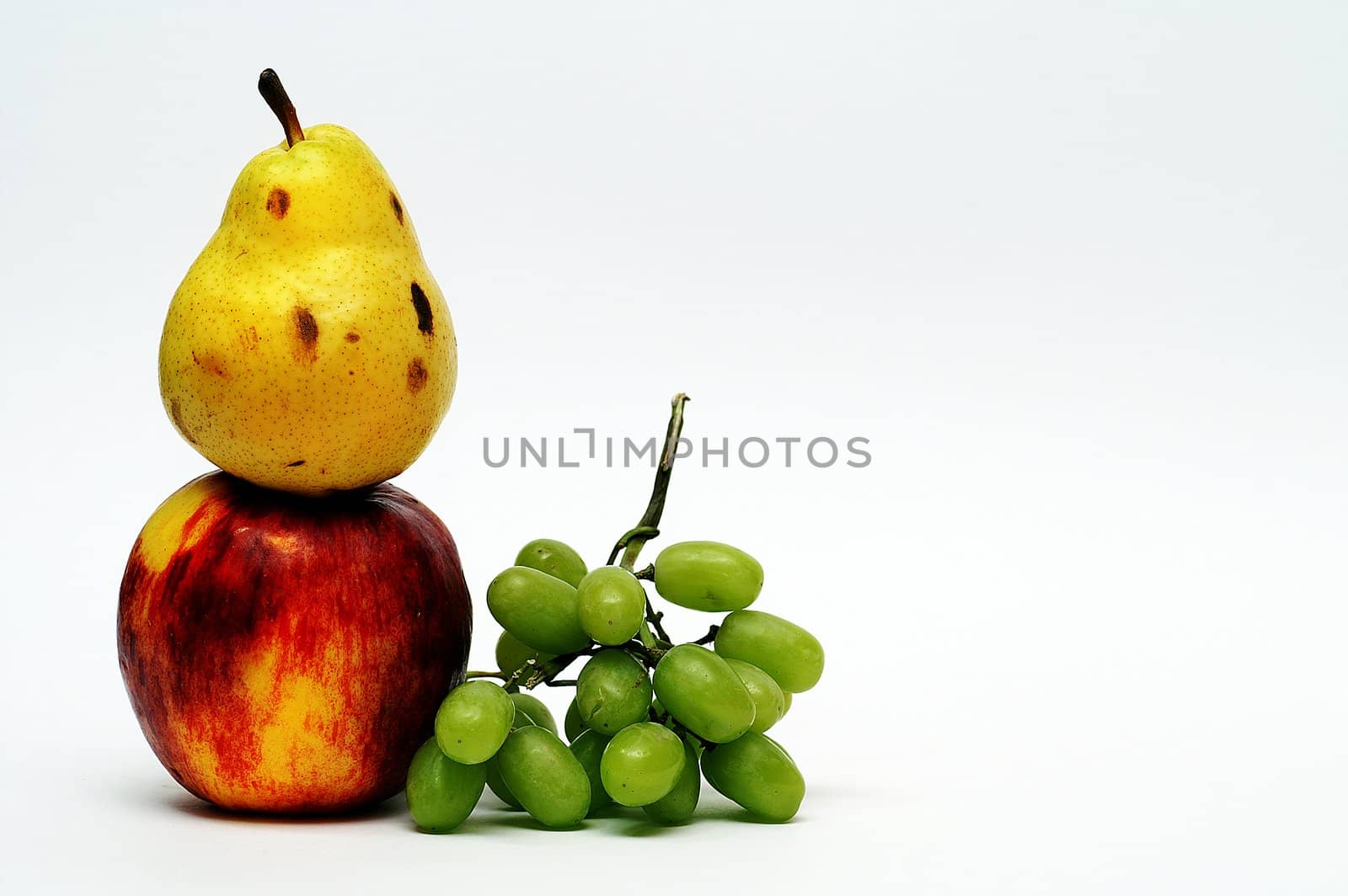 Yellow pear on top of red apple and green grape on white