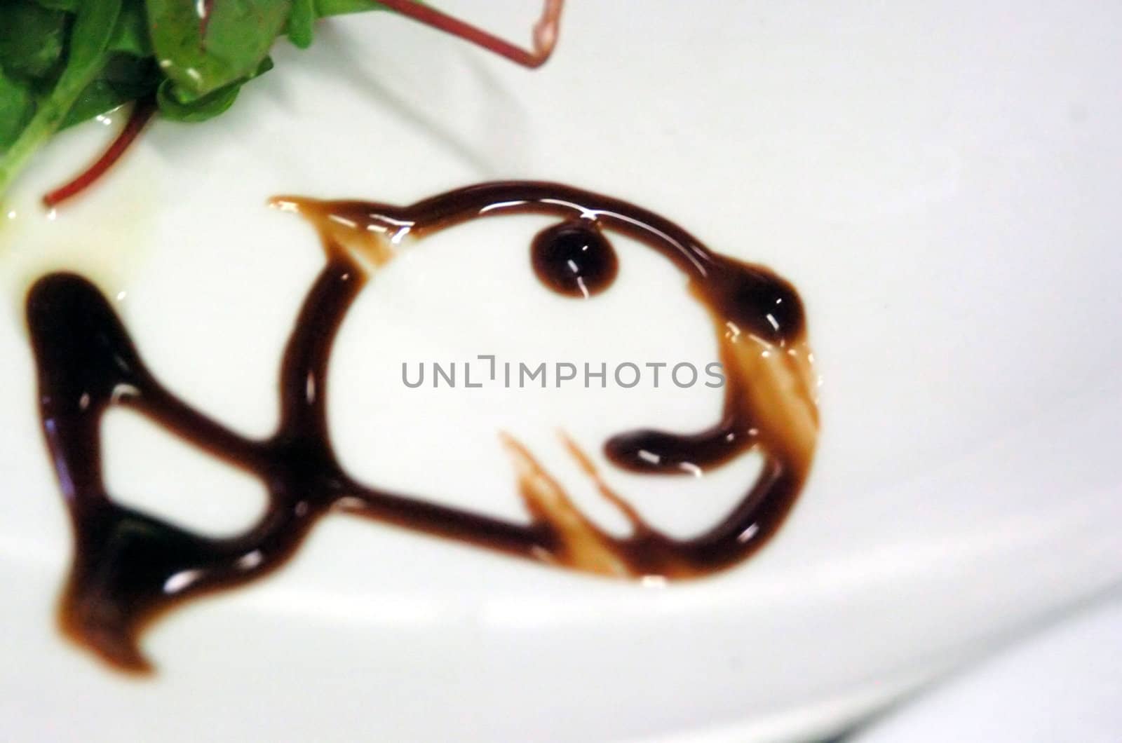 balsamico vinagre decoration in fish form on a white plate with green salad leaves