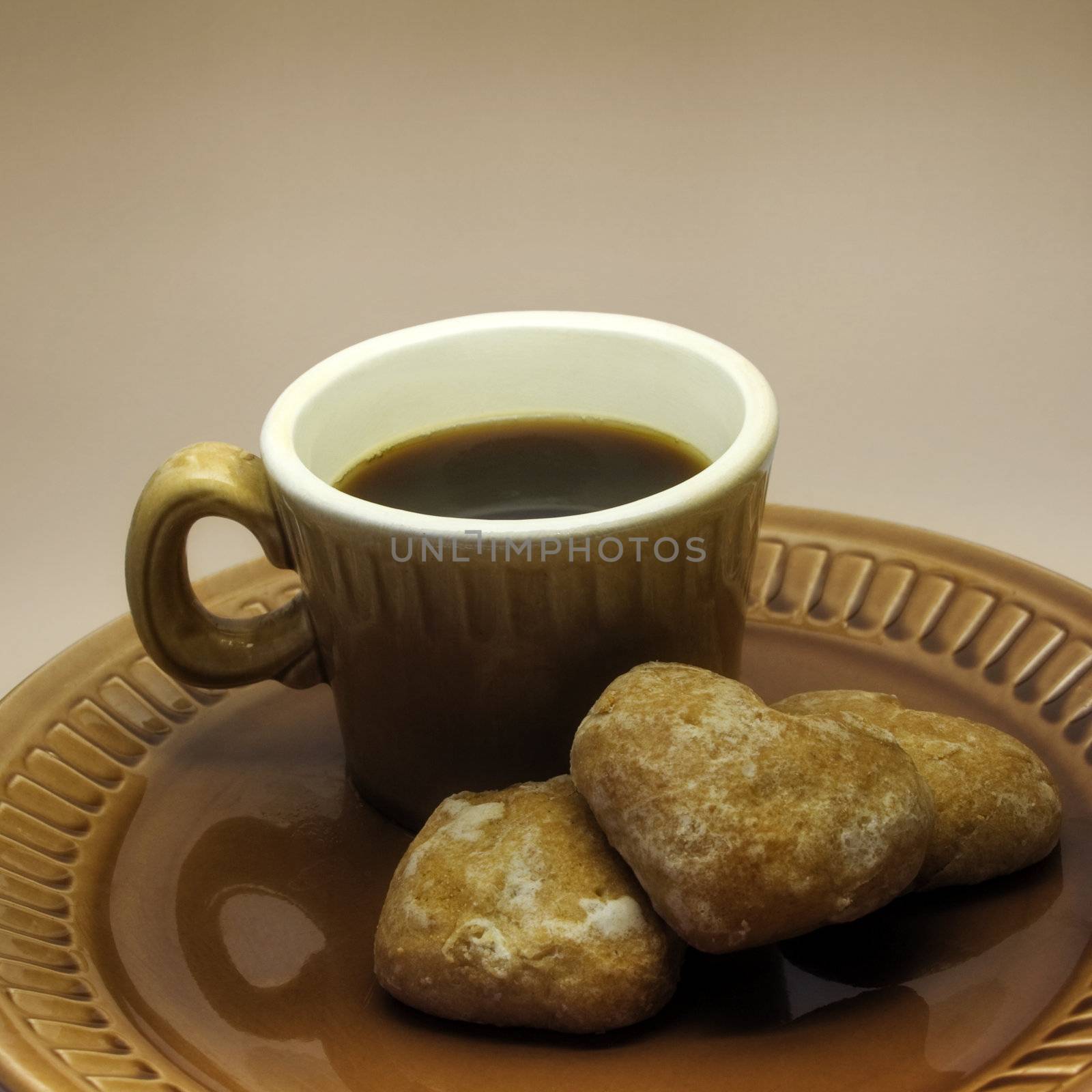 Cup of coffee and three heart-shape spice-cakes on a ceramic plate