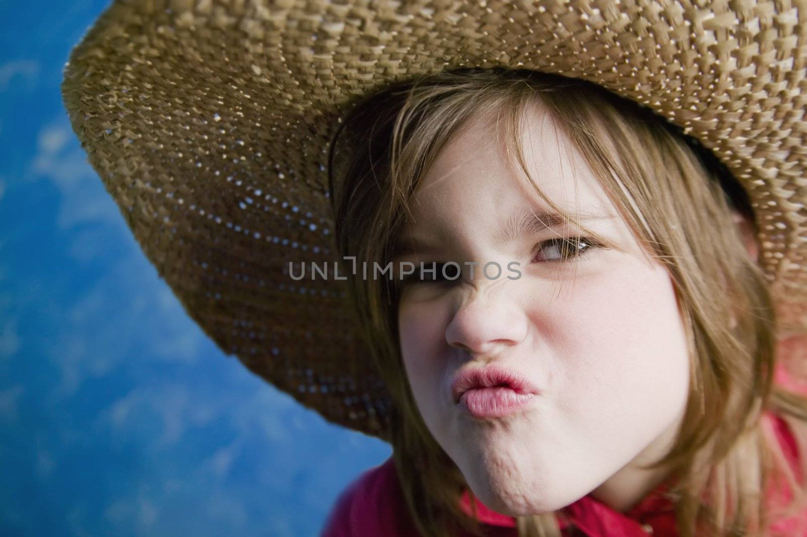 Little girl wearing a straw cowboy hat makes a funny face