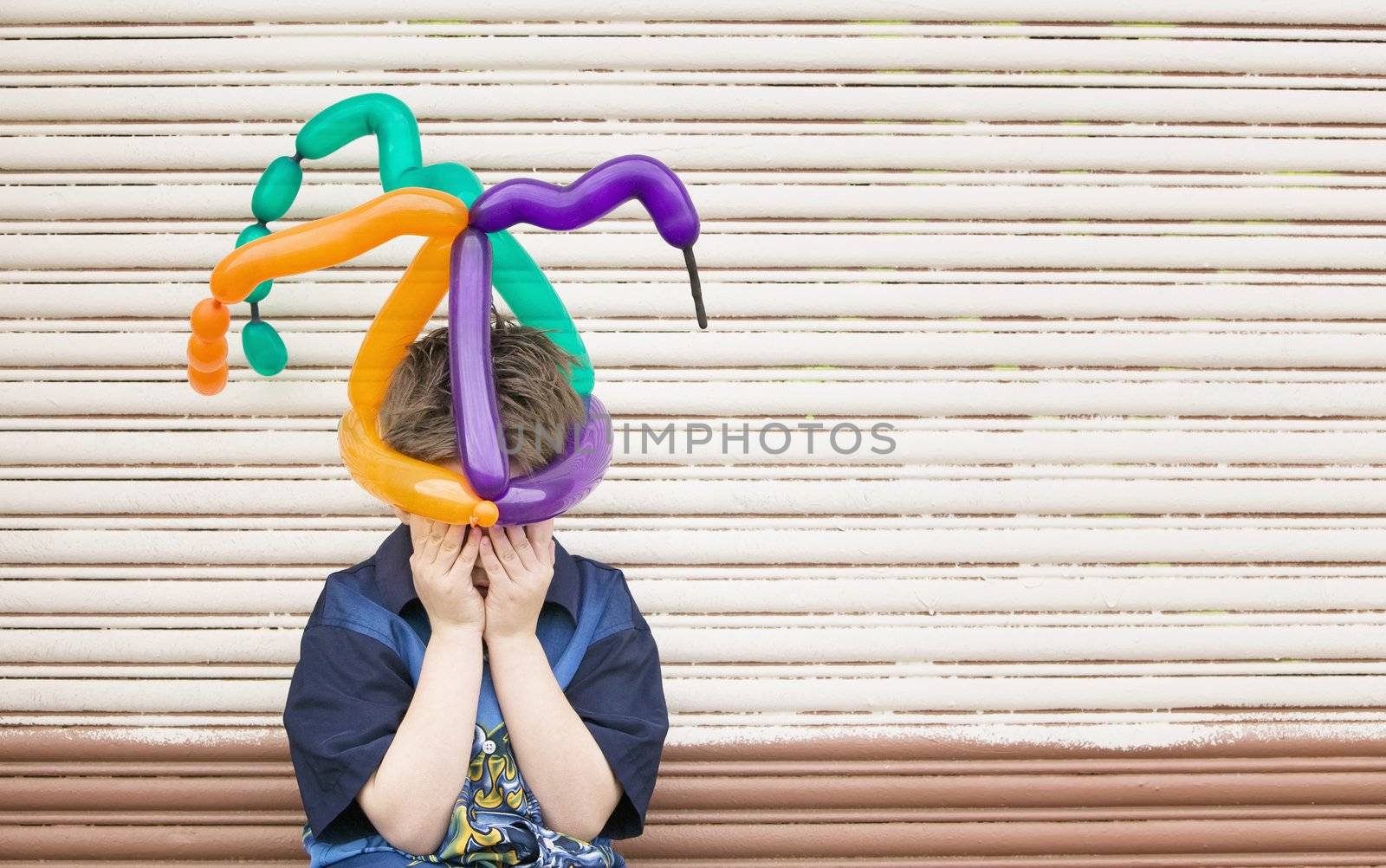 Young boy wearing a balloon hat hides his face