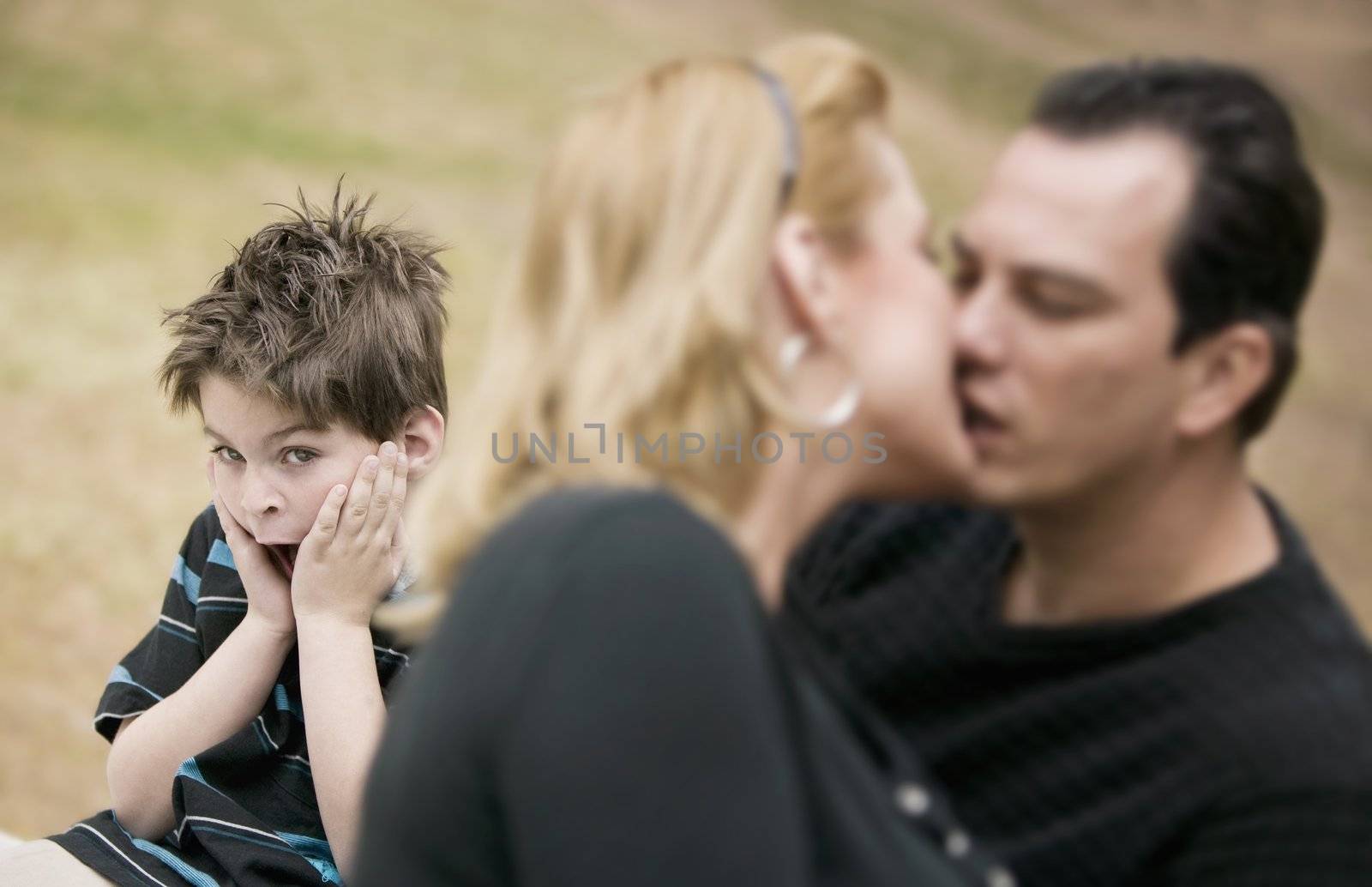 Horrified young boy with a kissing couple in the foreground