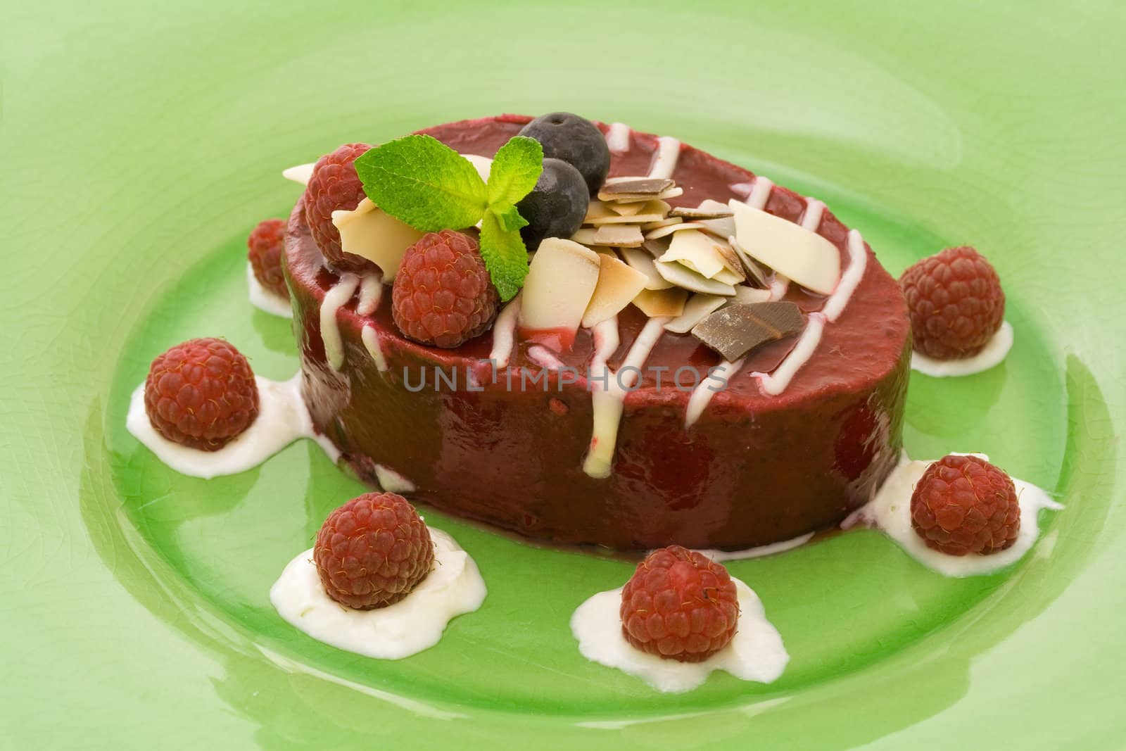 Raspberry mousse cake with whipped cream and fruits on a green plate