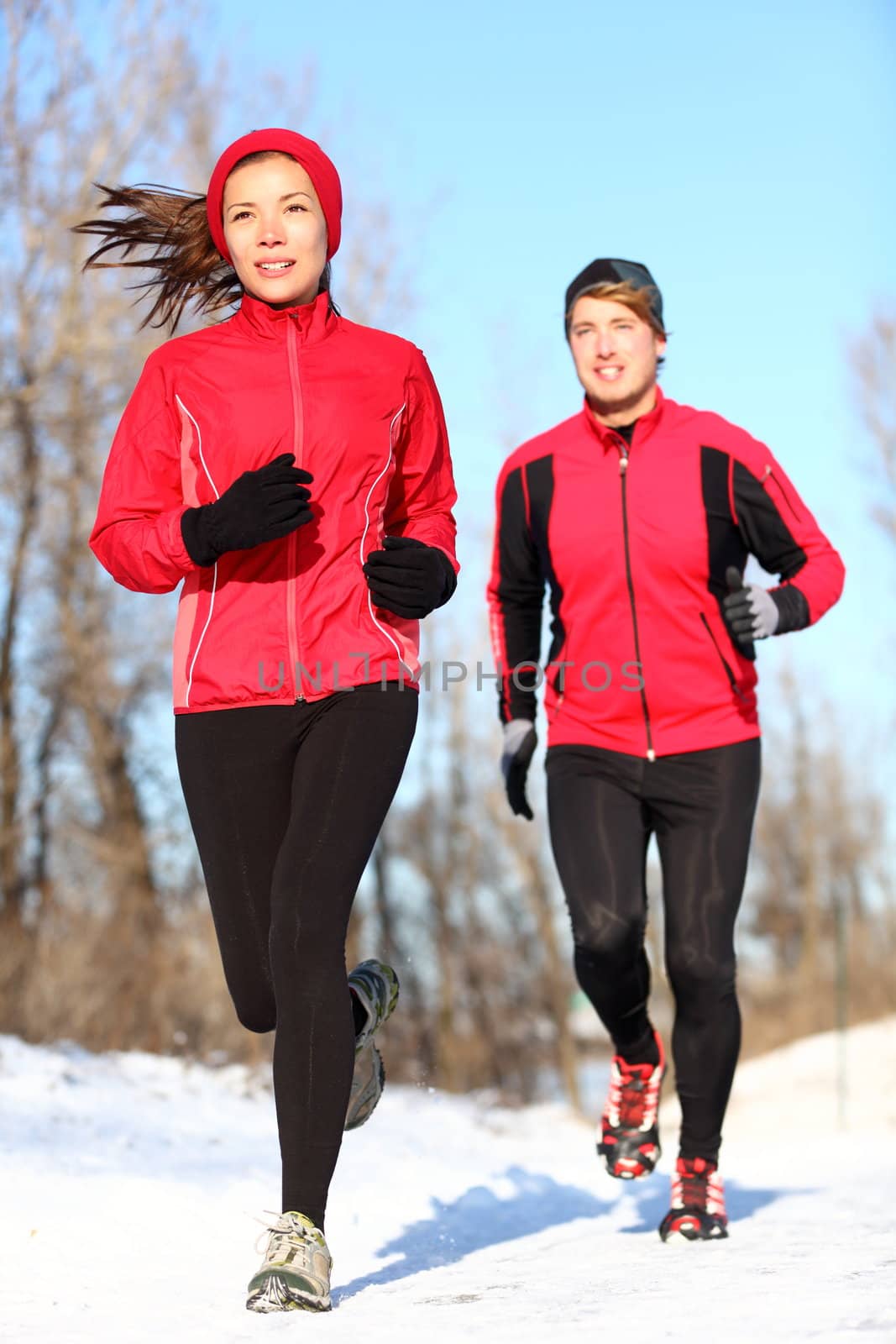 Sport couple running in winter snow. Woman and man runners jogging outdoors. Healthy fitness lifestyle concept with happy smiling young multiracial couple.