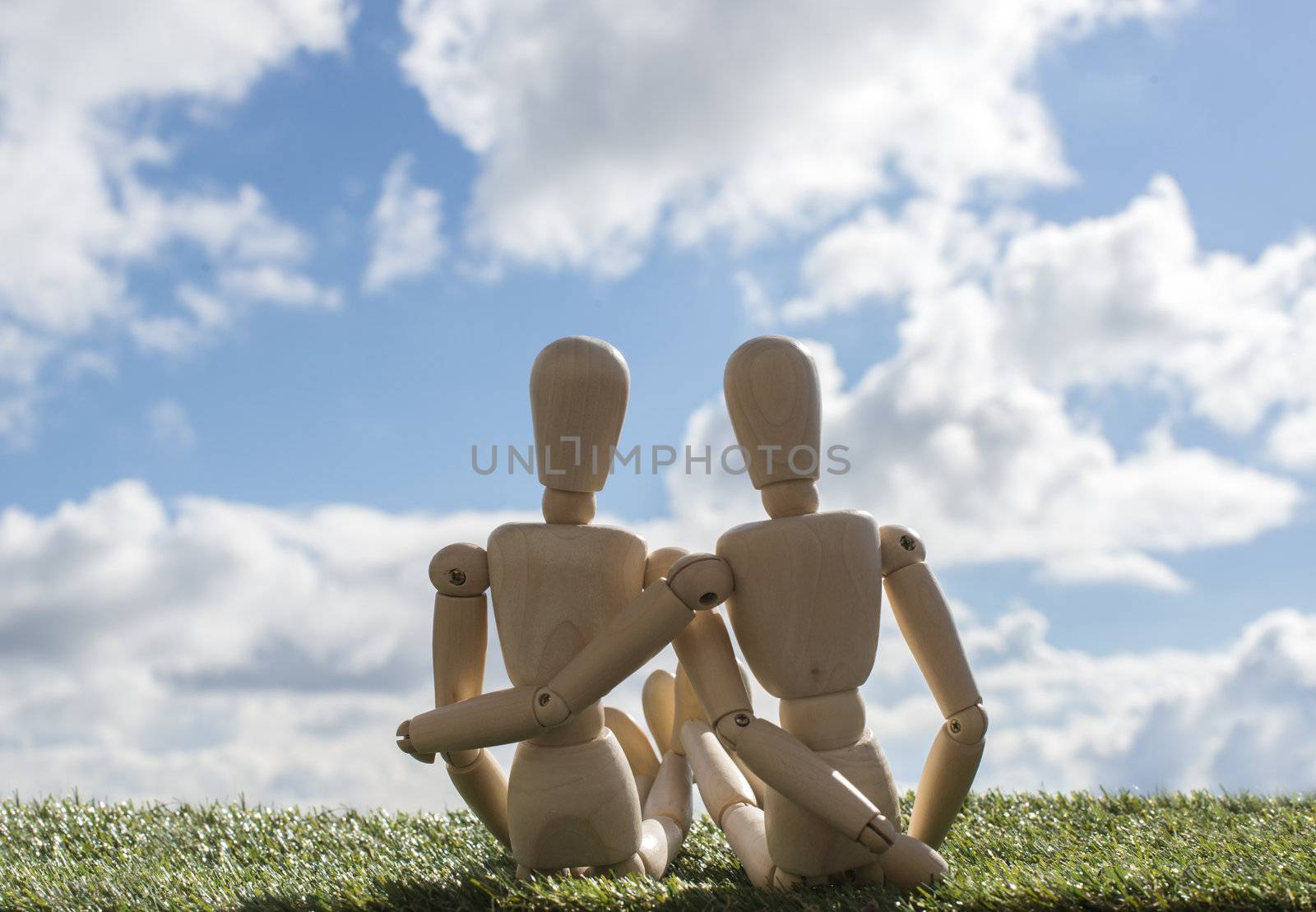 two wooden puppets as loving couple outside on green grass with blue sky