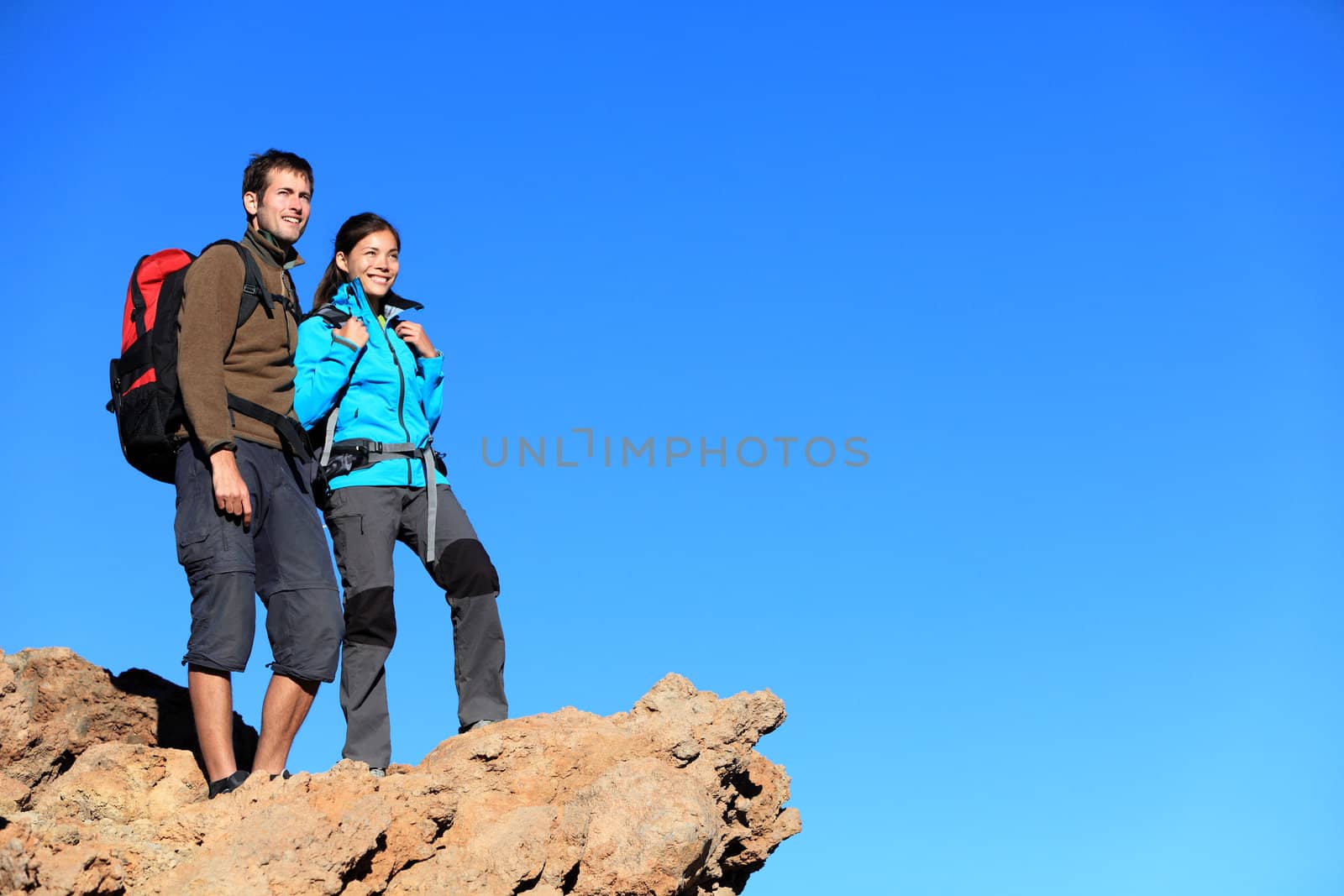 Hikers looking at view. Hiking young couple enjoying view looking at blue sky during hike. Multiracial couple with a lot of copy space.