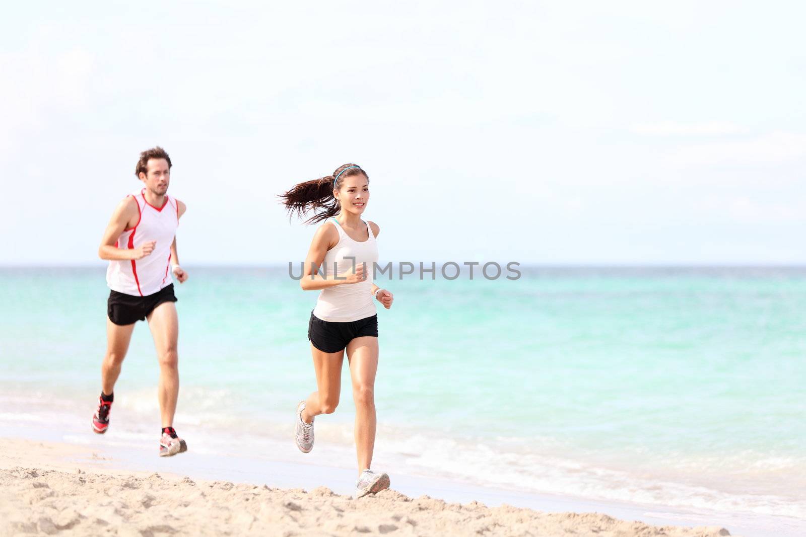 Couple running on beach. Runners jogging outside training. Caucasian / Asian woman runner and Caucasian fitness man model.