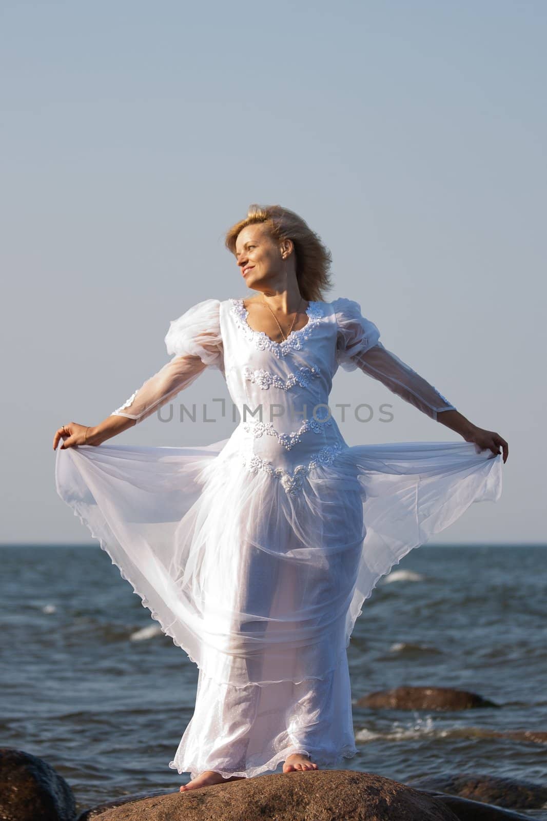 woman in white dress standing on a stone seaside